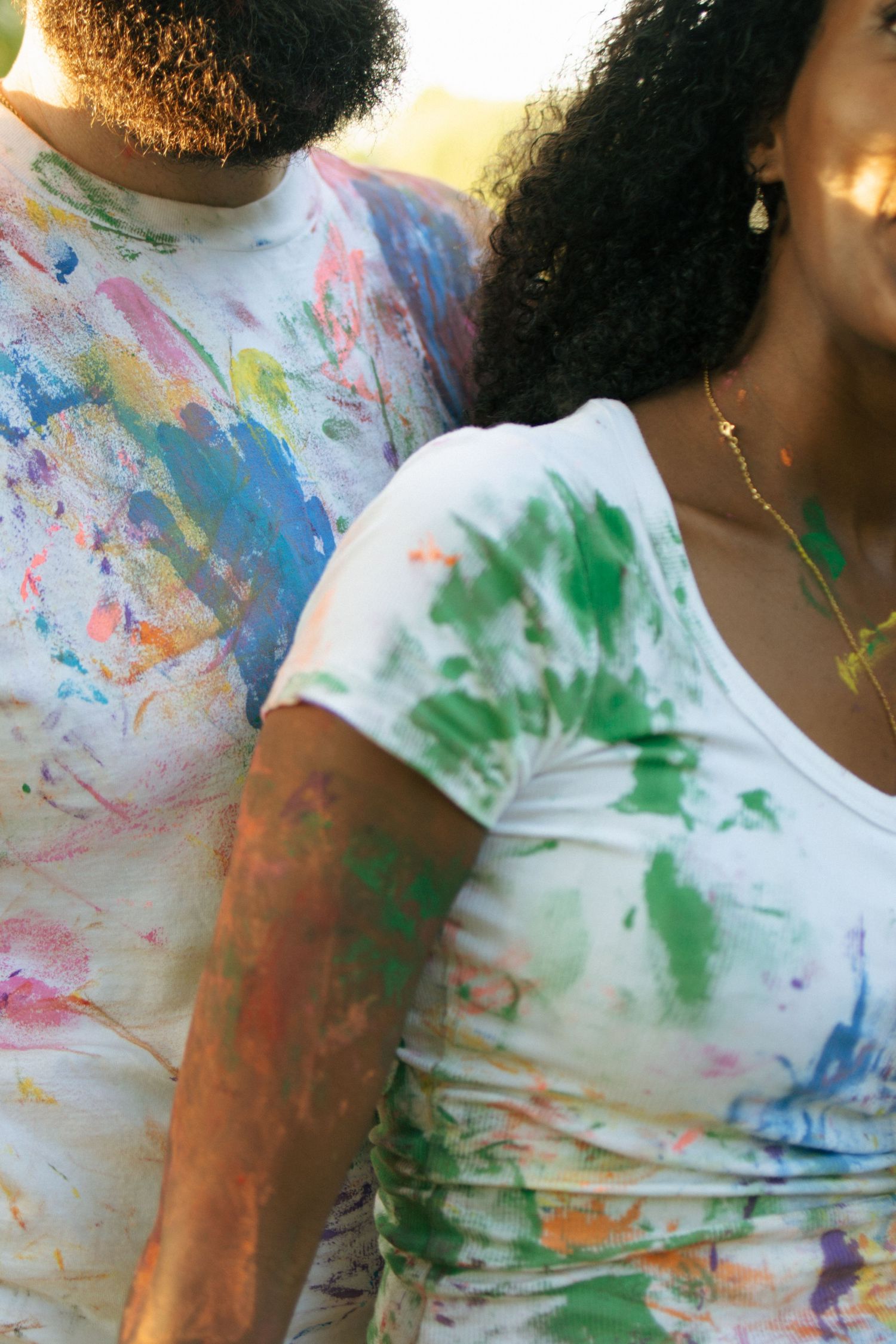 Close-up of a couple in colorful paint-splattered white t-shirts standing together outdoors.