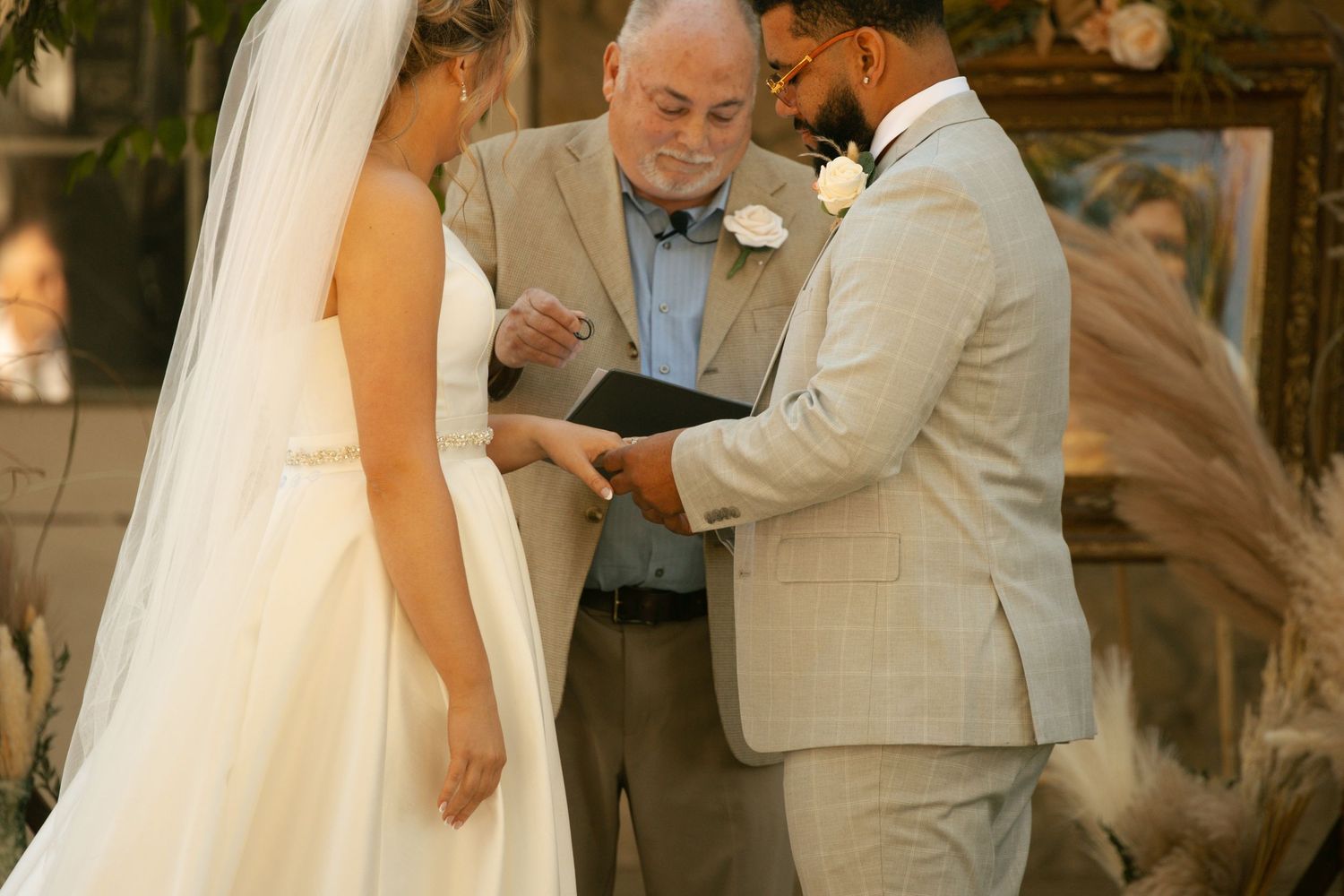 Officiant reads vows as bride and groom exchange rings during an elegant indoor wedding ceremony.