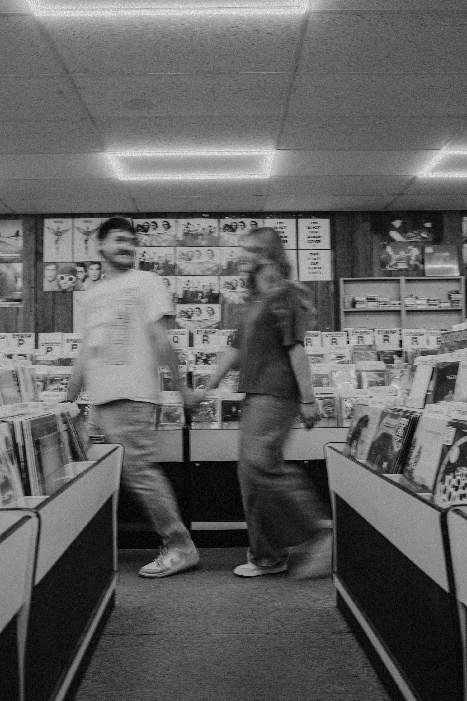 Black and white photo of two blurred people browsing vinyl records in a retro music store.