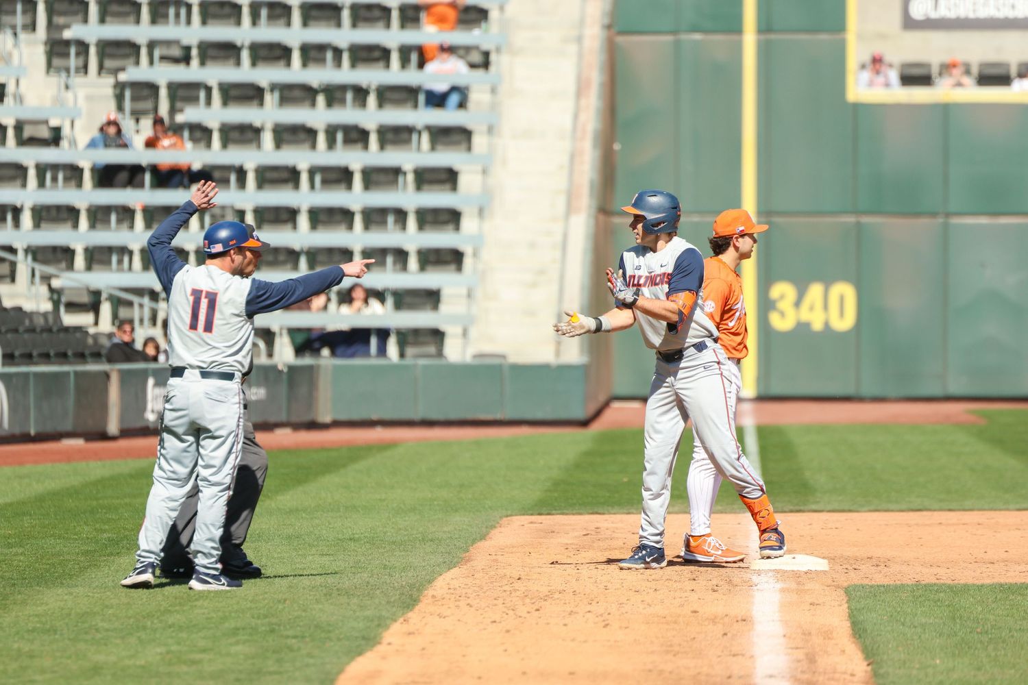 Baseball players interact during game with the '340' sign visible on outfield wall in sunny stadium.