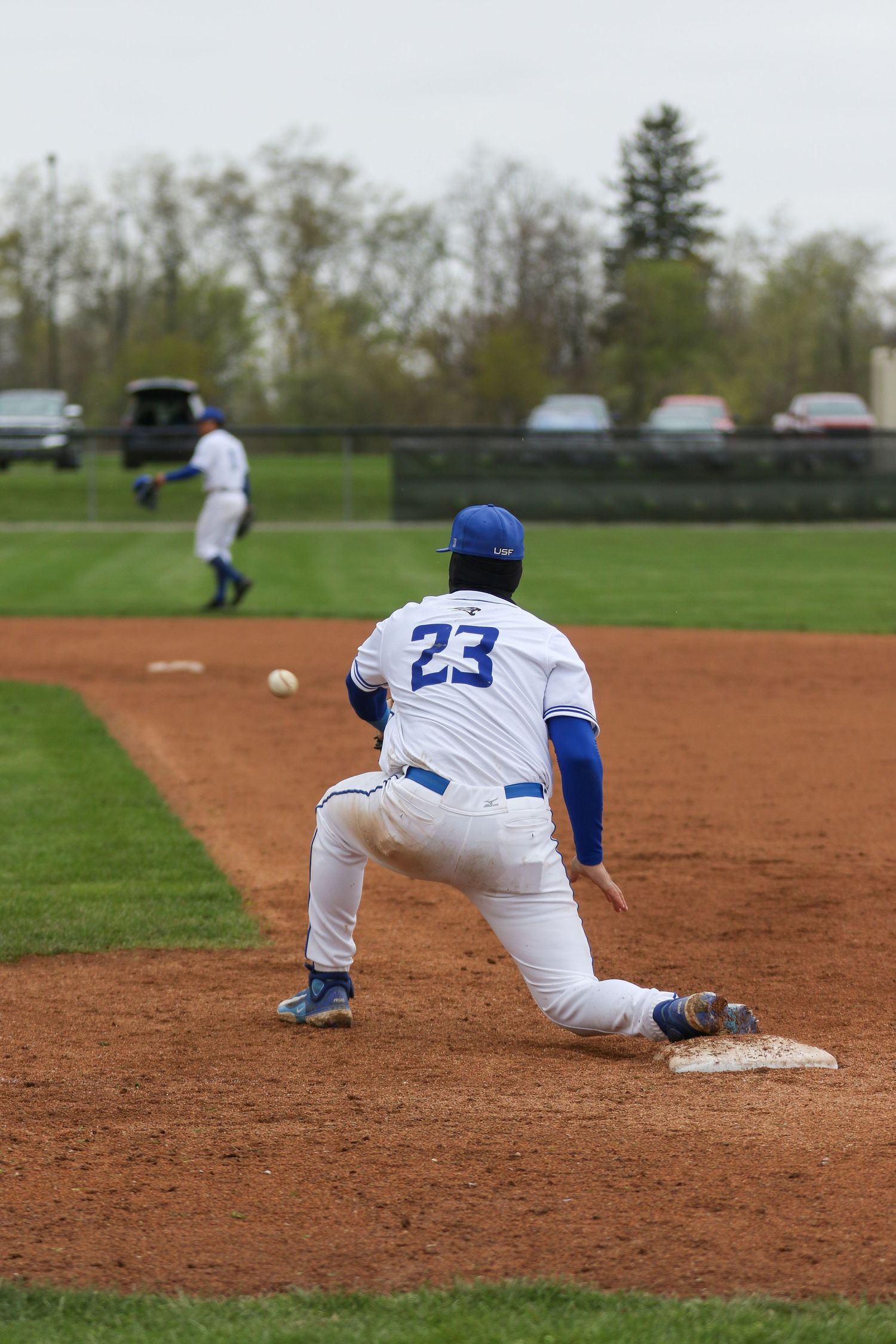 Baseball player in blue and white uniform #23 takes position at first base during a game on grass field.