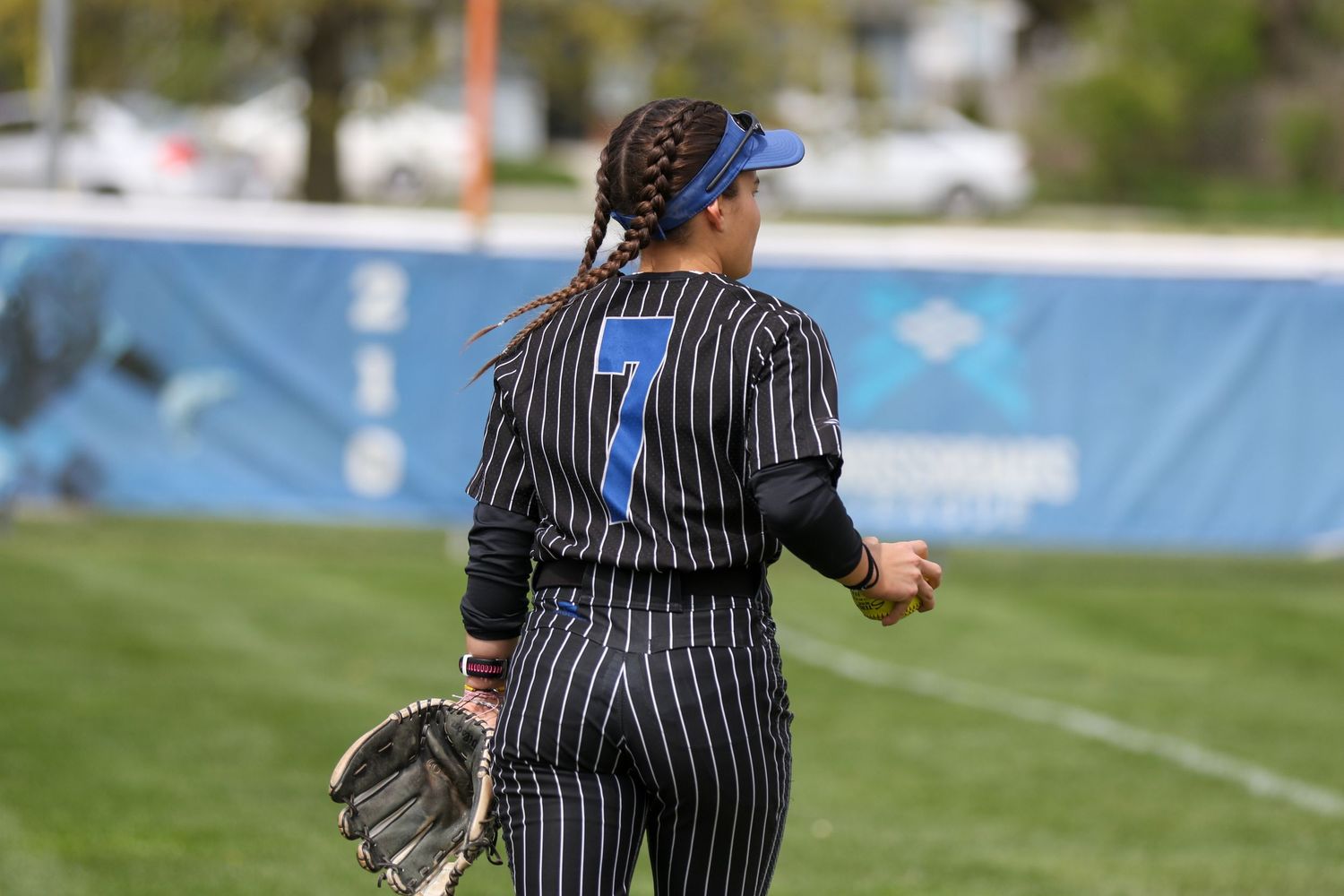A softball umpire in pinstriped uniform and blue cap stands on a field during a game.