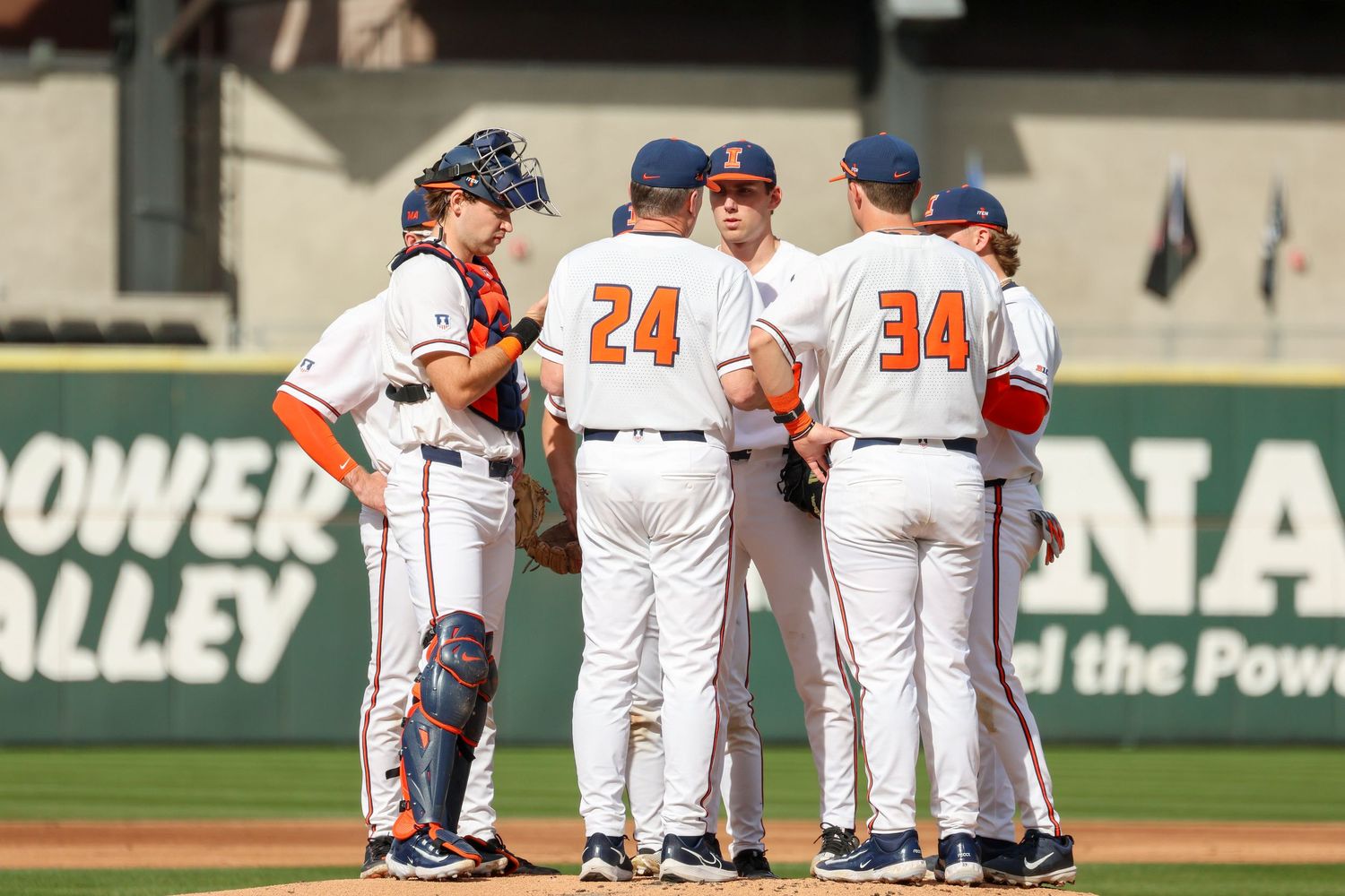 Baseball players huddle on the pitchers mound during a game at a stadium with Power Alley sign visible in background.