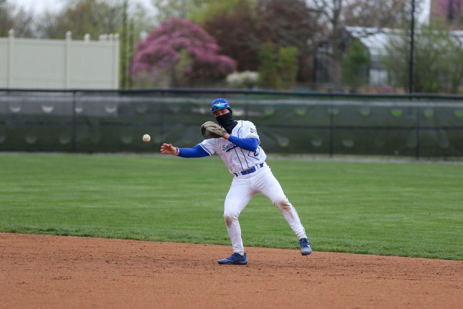Baseball player in white and blue uniform throws the ball on infield dirt during a game.