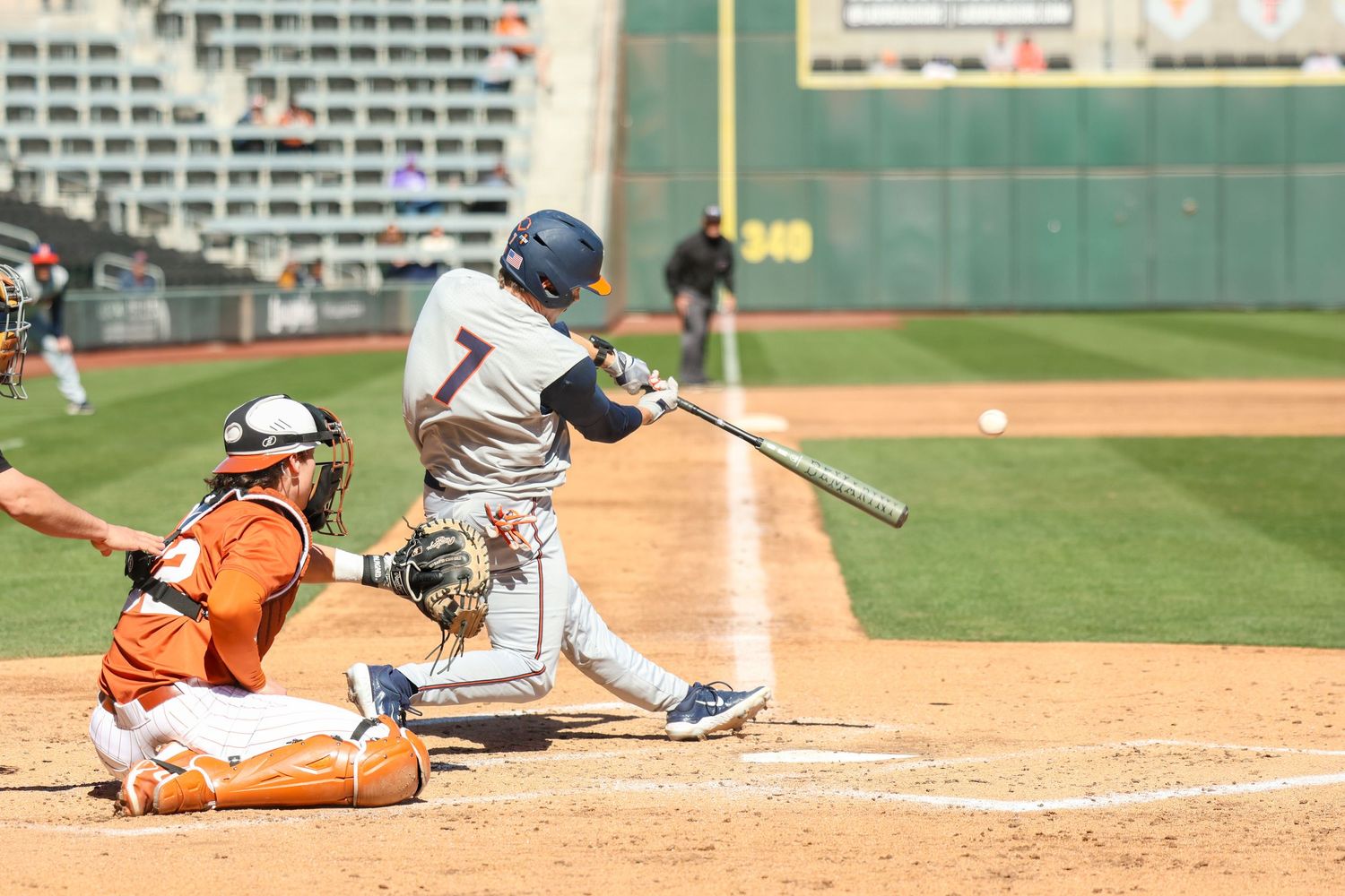 Baseball batter swings at home plate during game against orange-uniformed catcher at professional baseball stadium.