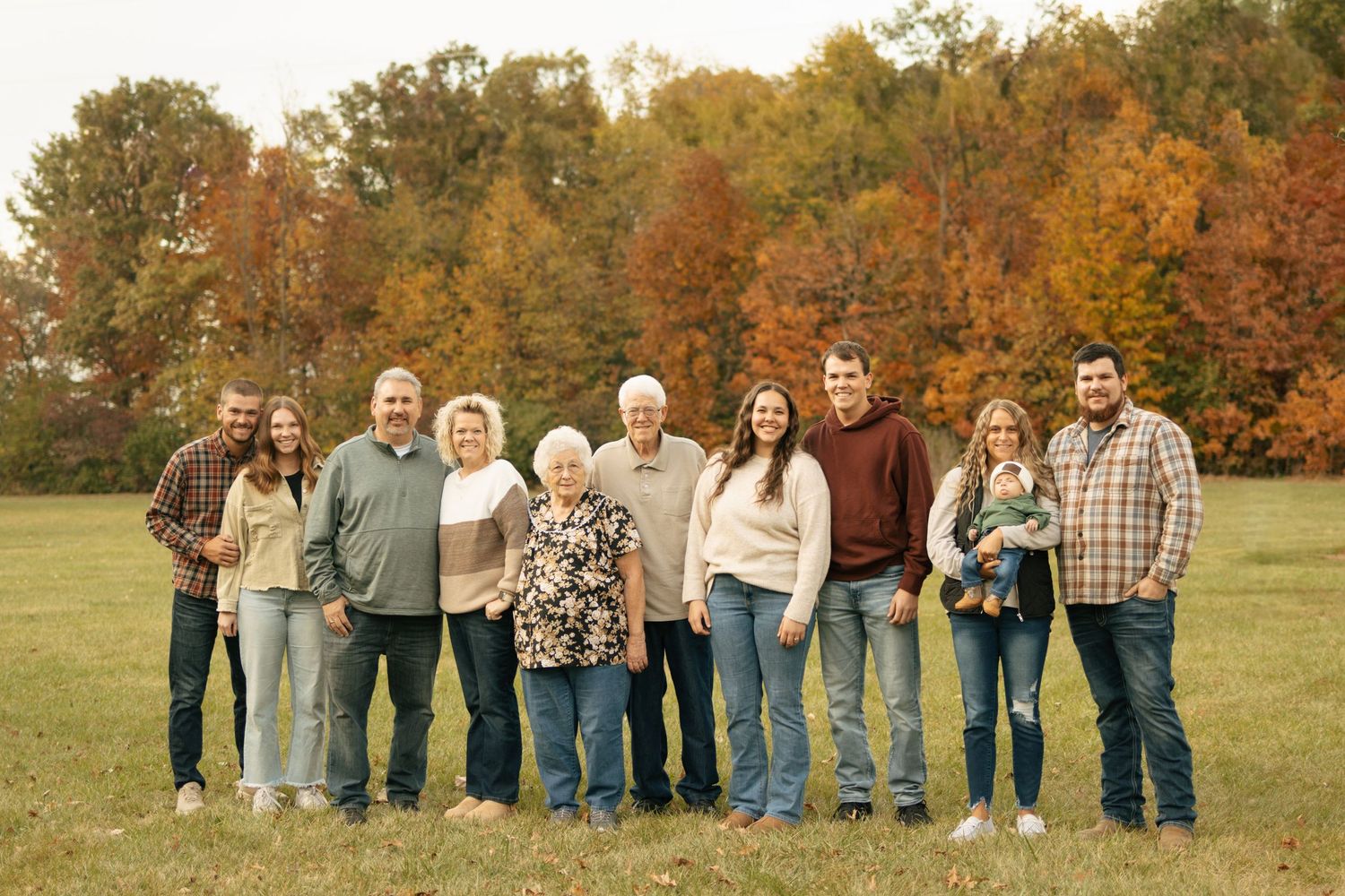 Multi-generational family portrait in autumn park with colorful fall foliage trees in background.