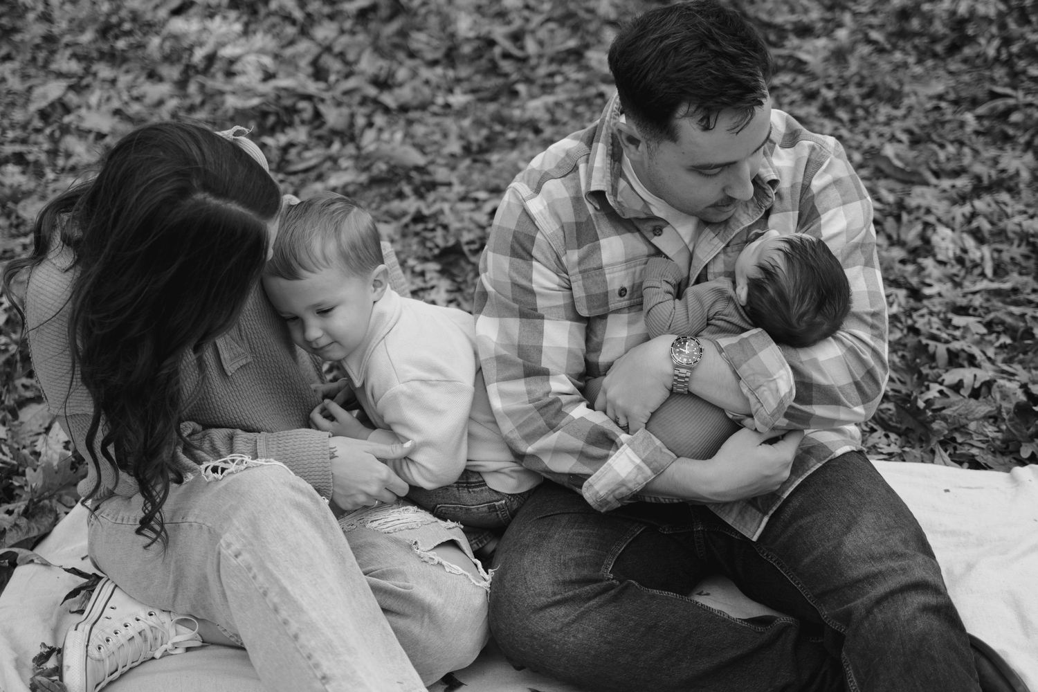 Black and white family photo of parents sitting outdoors with two young children, sharing a warm and loving moment.