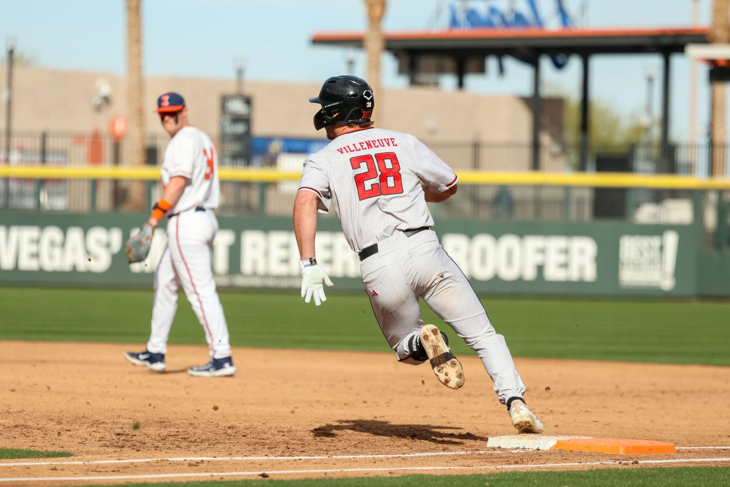Baseball player in white uniform with number 28 rounds first base during a game on a sunny day at a stadium.