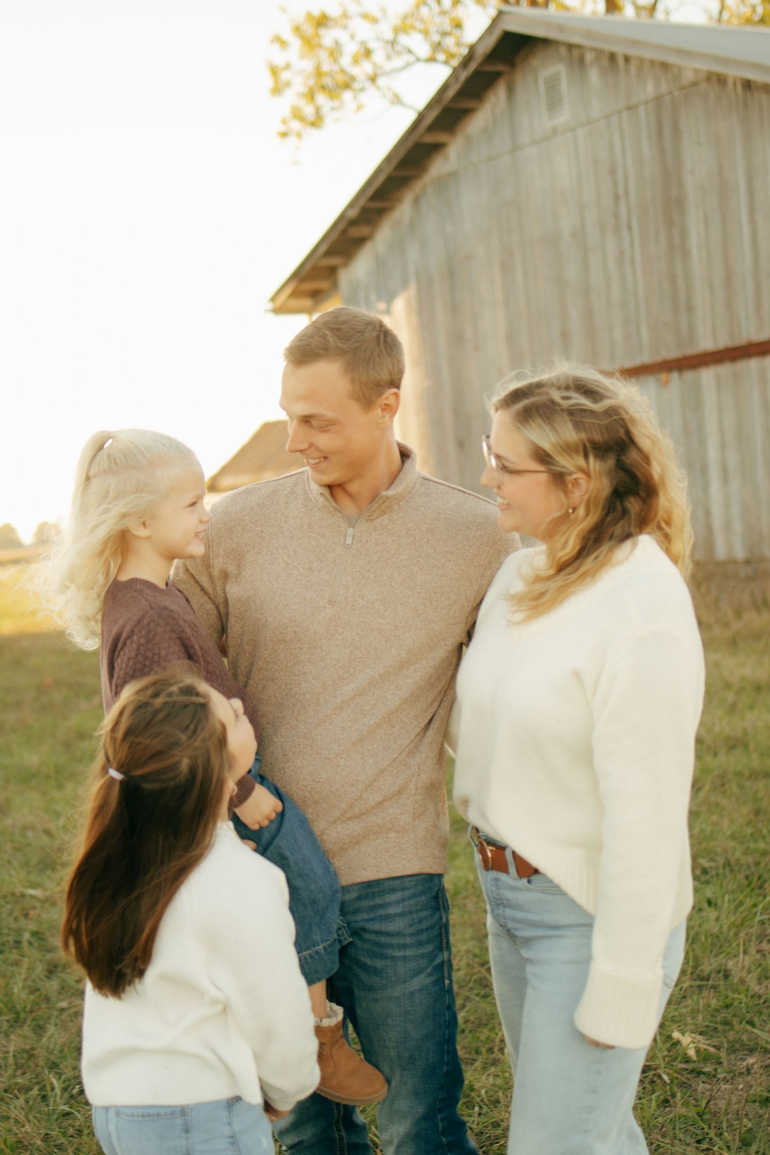 Family of four sharing a warm moment outdoors near a rustic barn during golden hour.