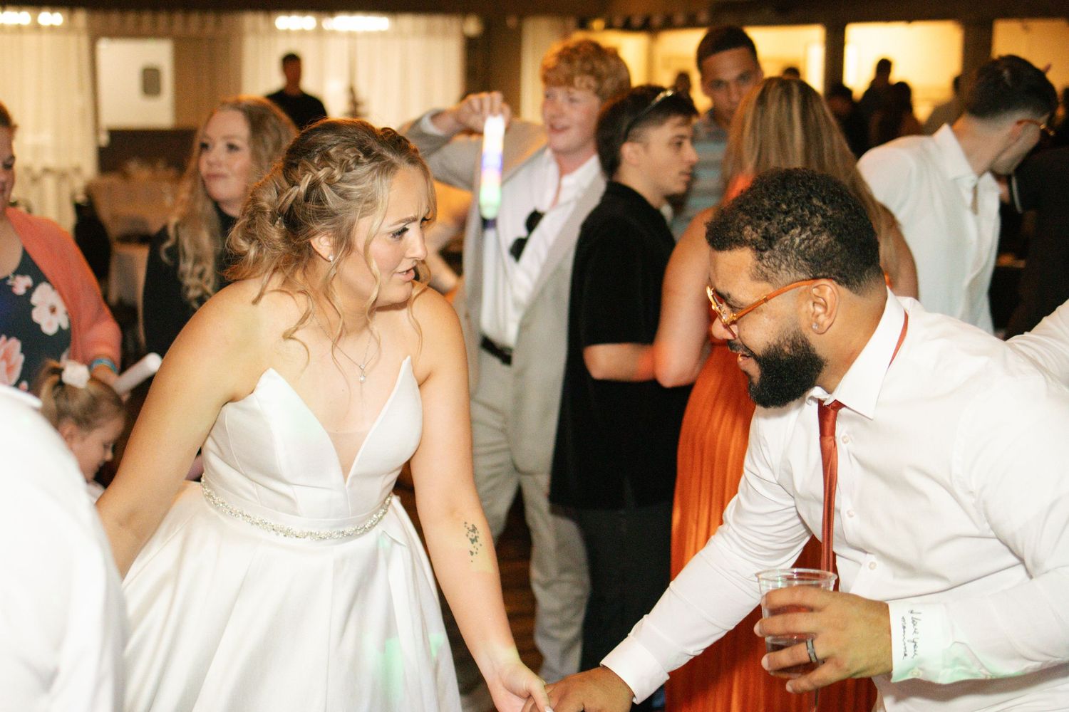 Bride and groom dancing joyfully together at wedding reception surrounded by guests on dance floor.