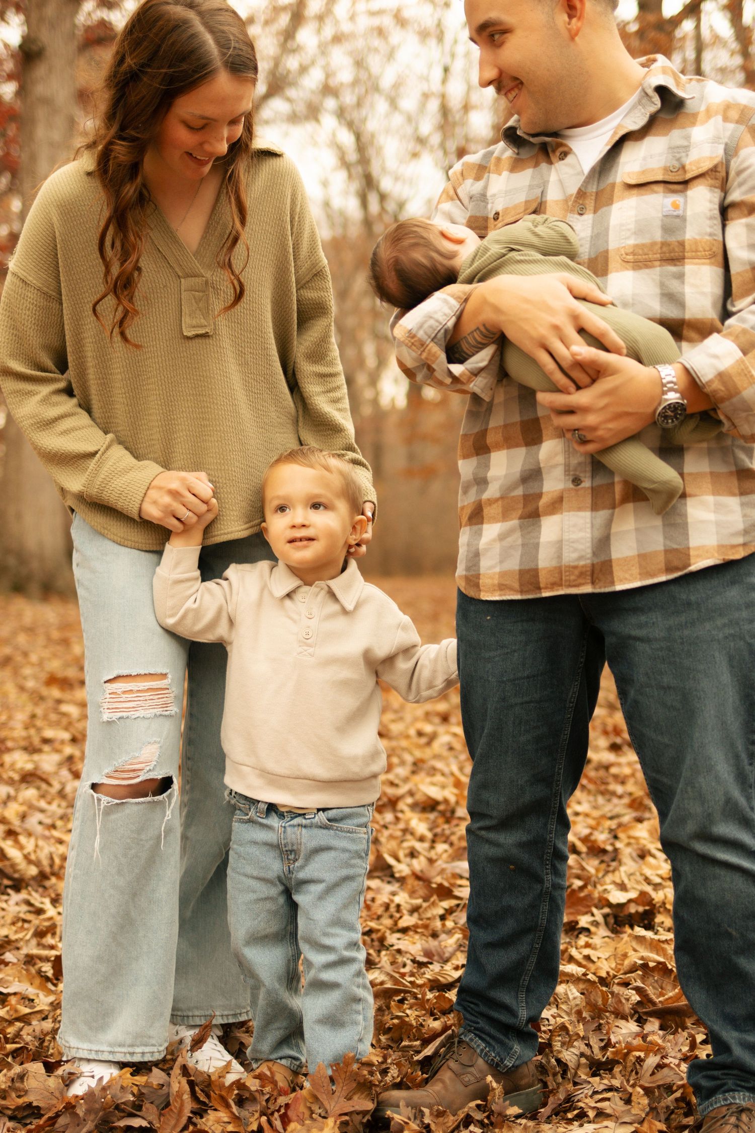 Young family with toddler and newborn posing together in fall leaves in a woodland setting.