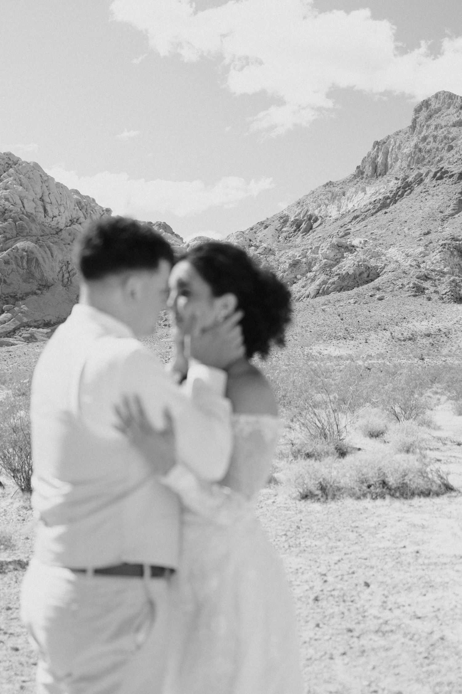 A romantic couple shares intimate moments in a desert landscape with rugged mountains in the background.