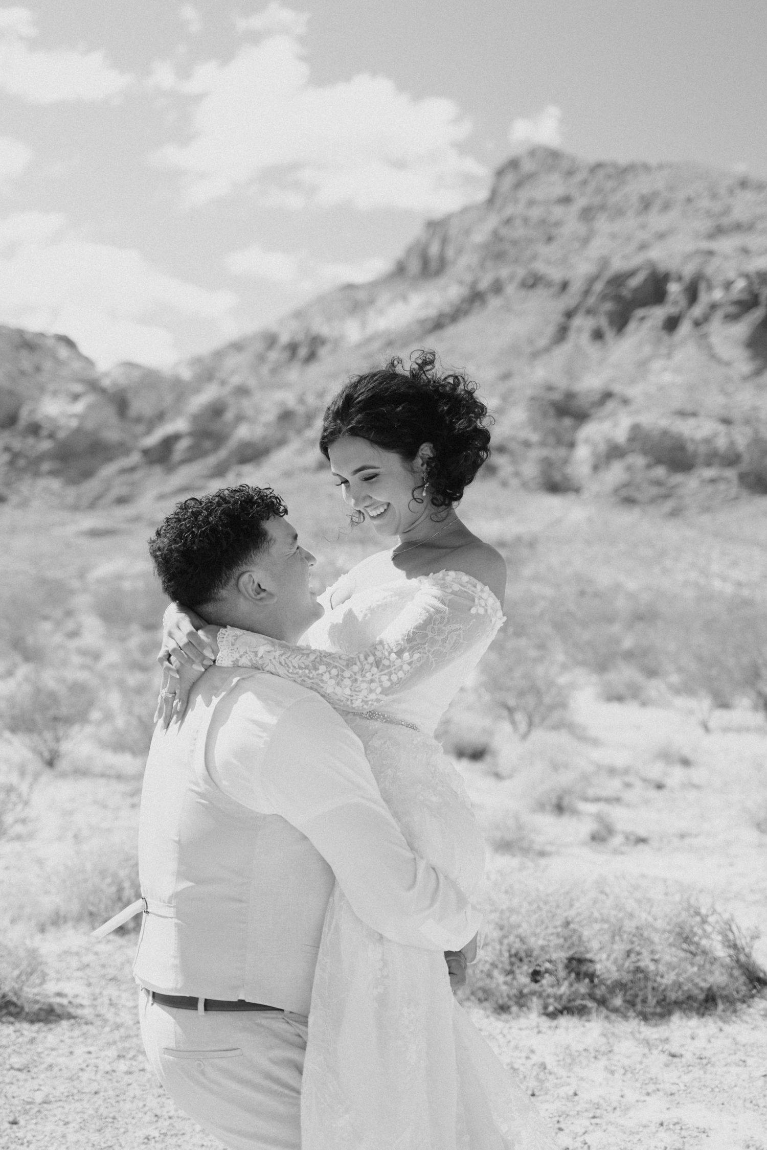 A black and white photo captures a romantic couple laughing together in a desert landscape.