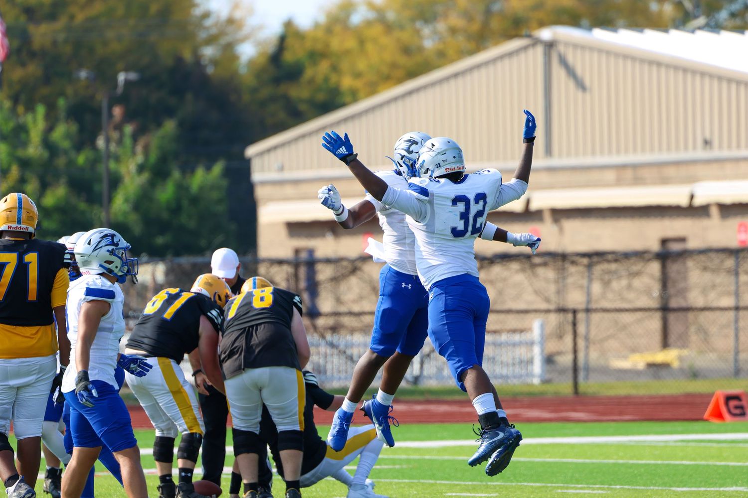 Football players jump in celebration during a game between blue and black uniformed teams on the field.