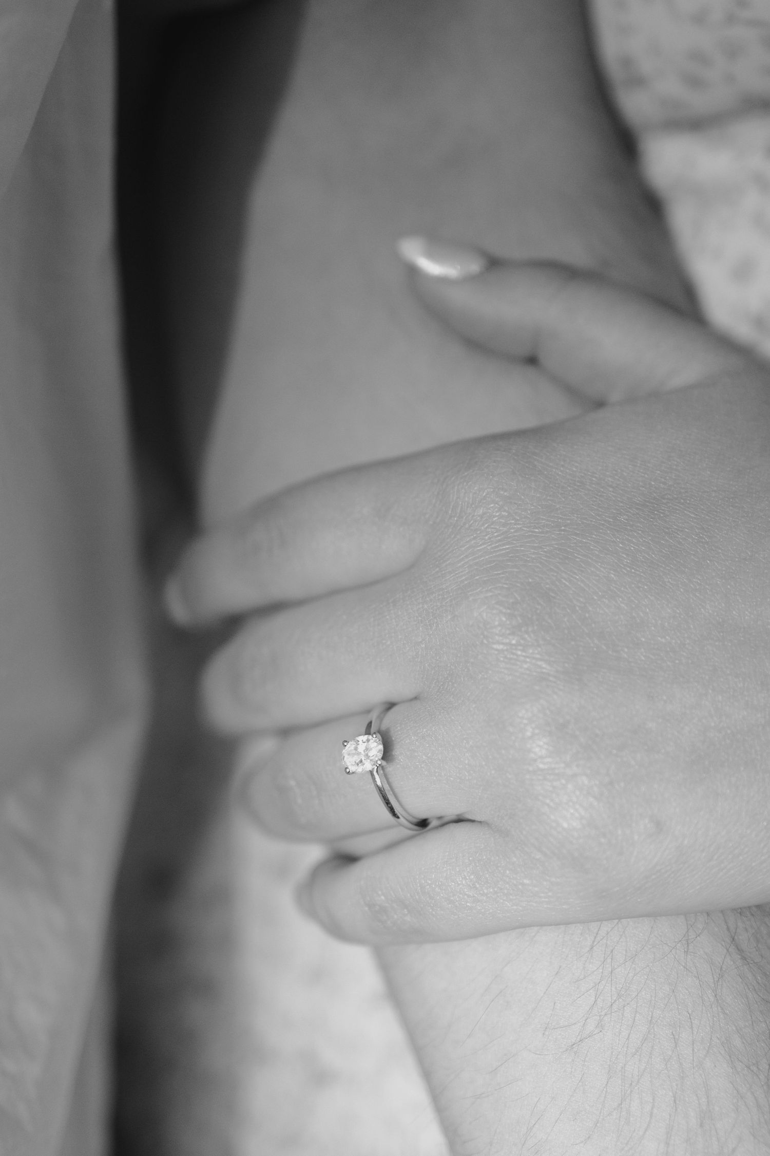 Black and white close-up of a hand wearing a solitaire diamond engagement ring.