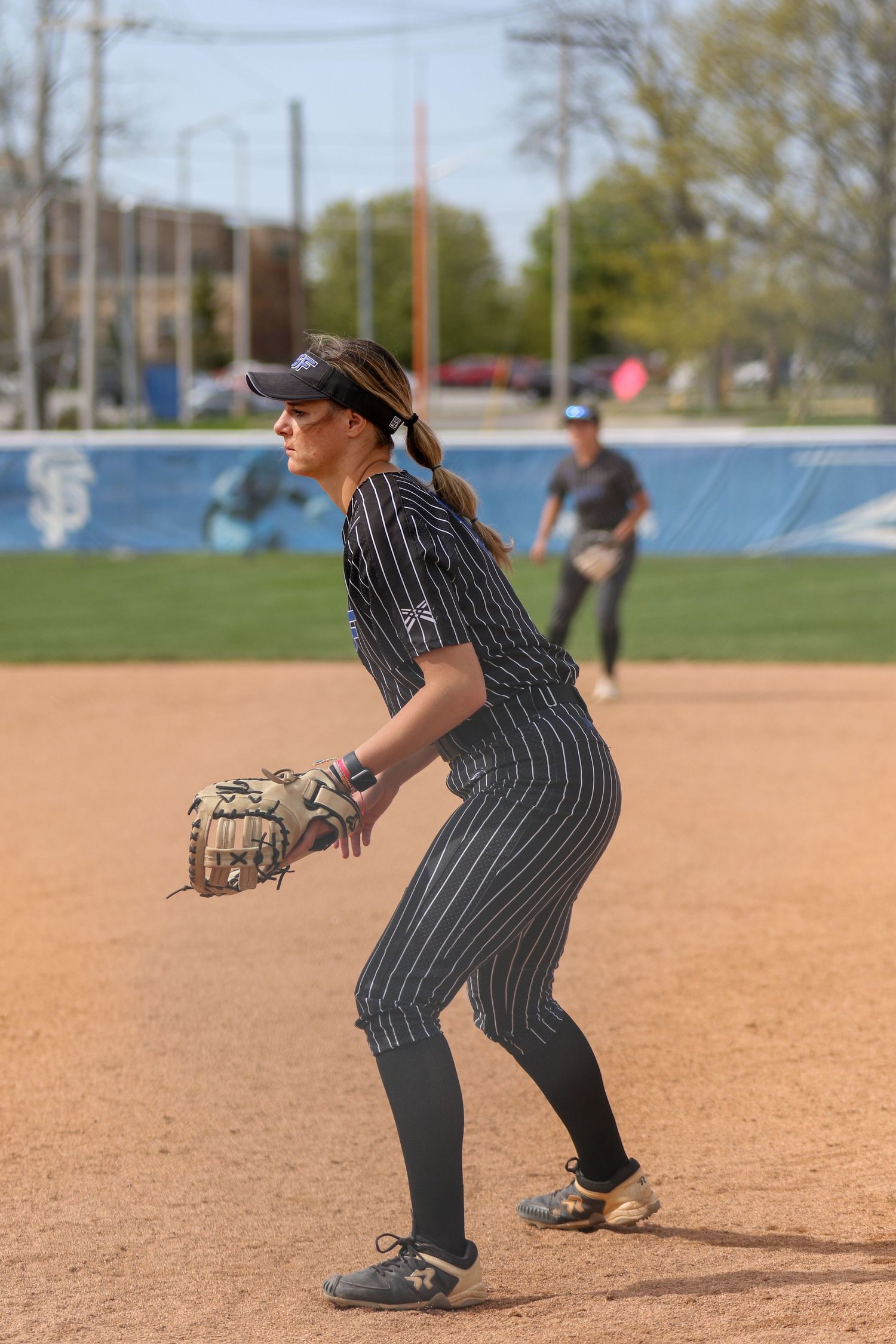 Softball player in pinstriped uniform stands ready in fielding position on dirt infield during game.