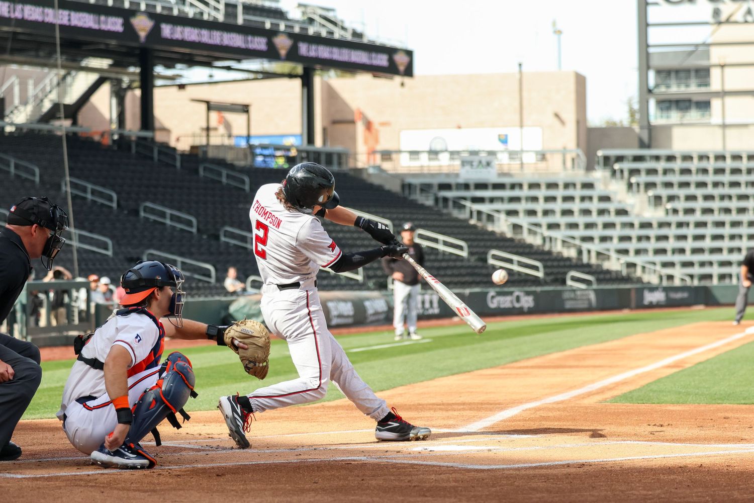 Baseball batter swings at pitch during game at empty stadium with catcher crouched behind home plate.