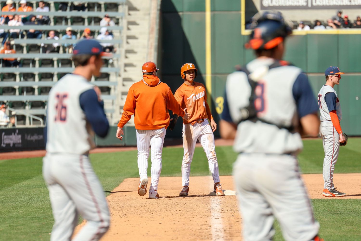 A baseball game in progress with players and coaches on the field during a sunny day at the ballpark.