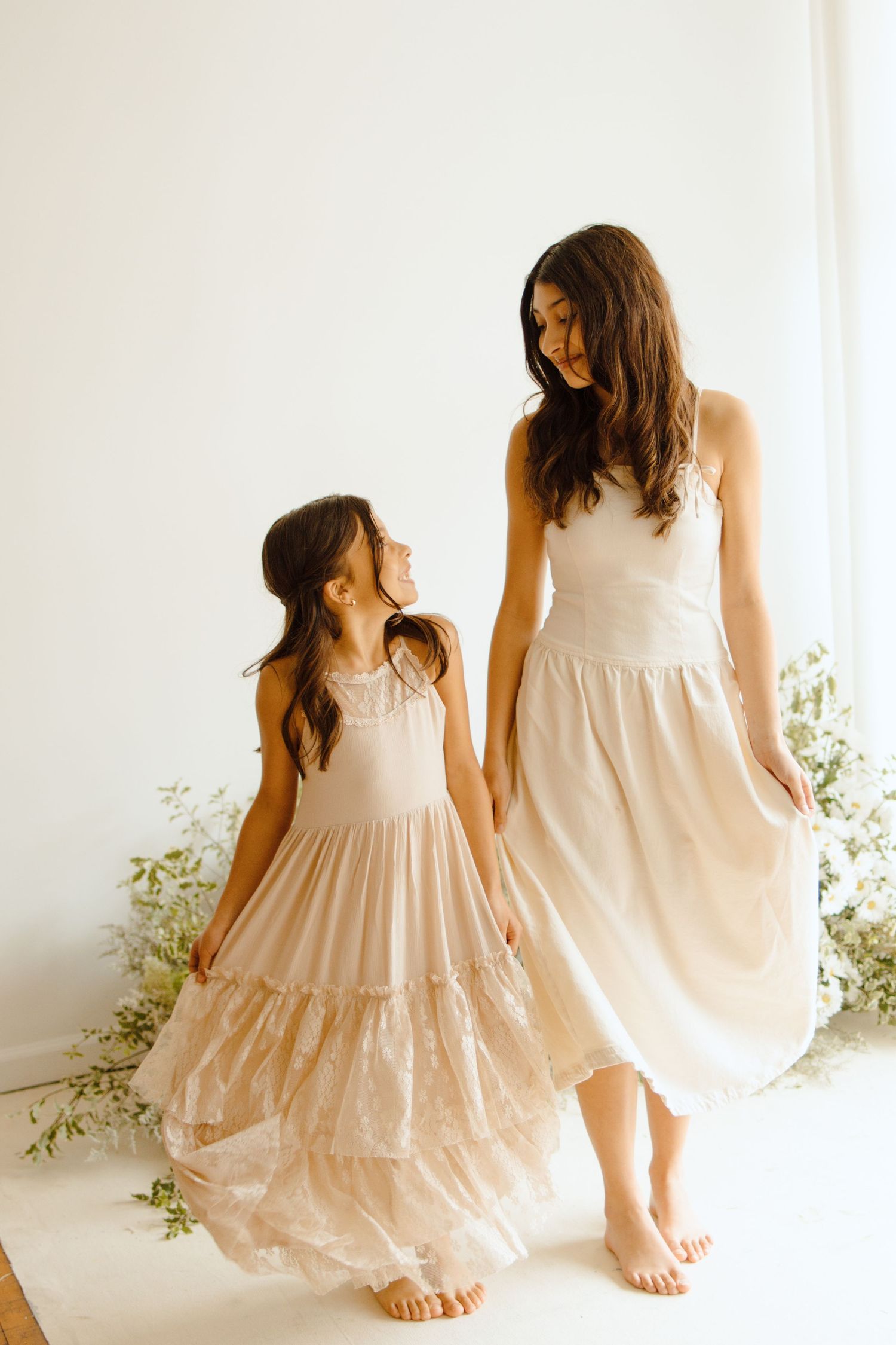 A woman and young girl in matching blush tiered dresses pose together in a bright white studio setting.