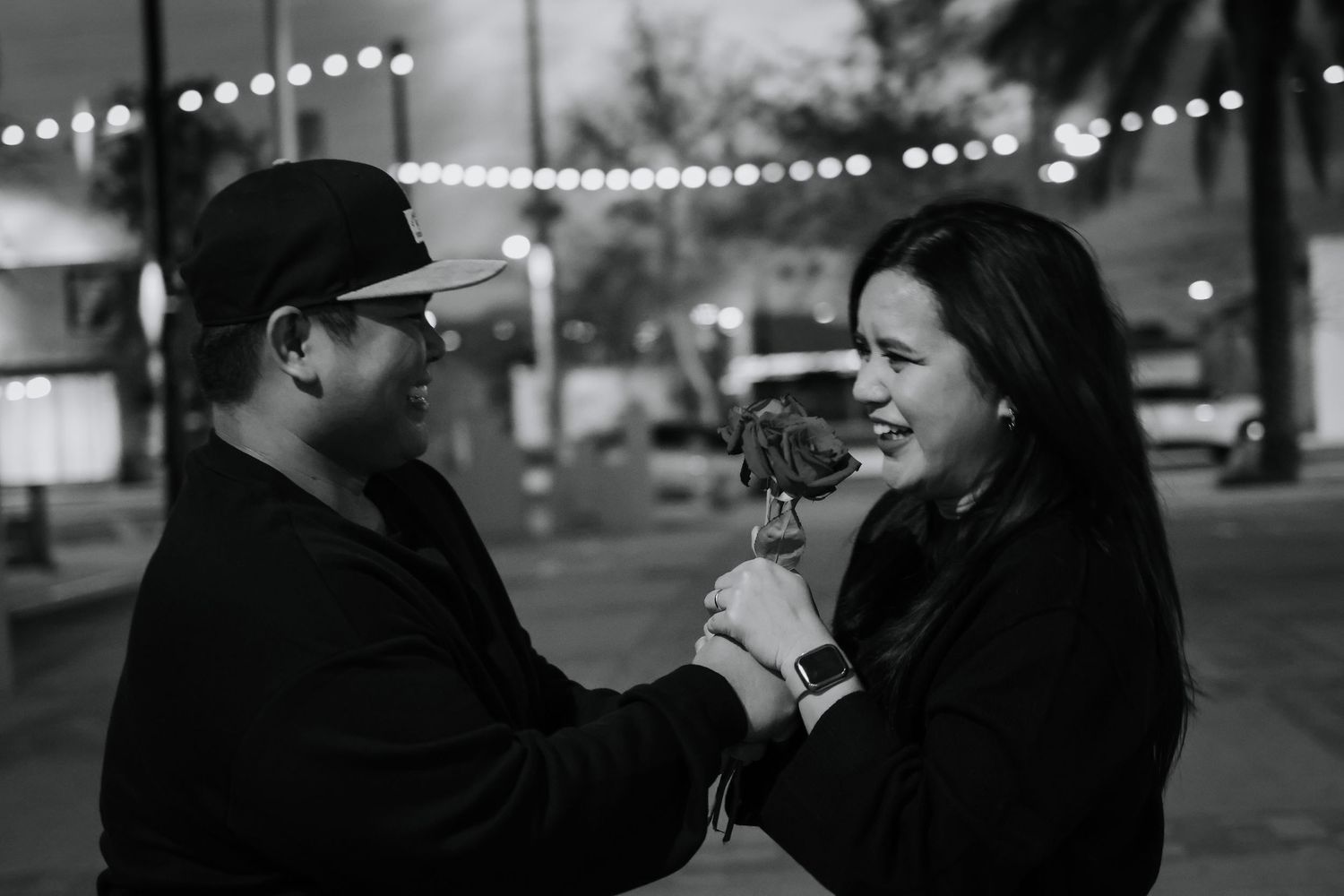 Black and white photo series showing two people sharing intimate moments outdoors with string lights in background.