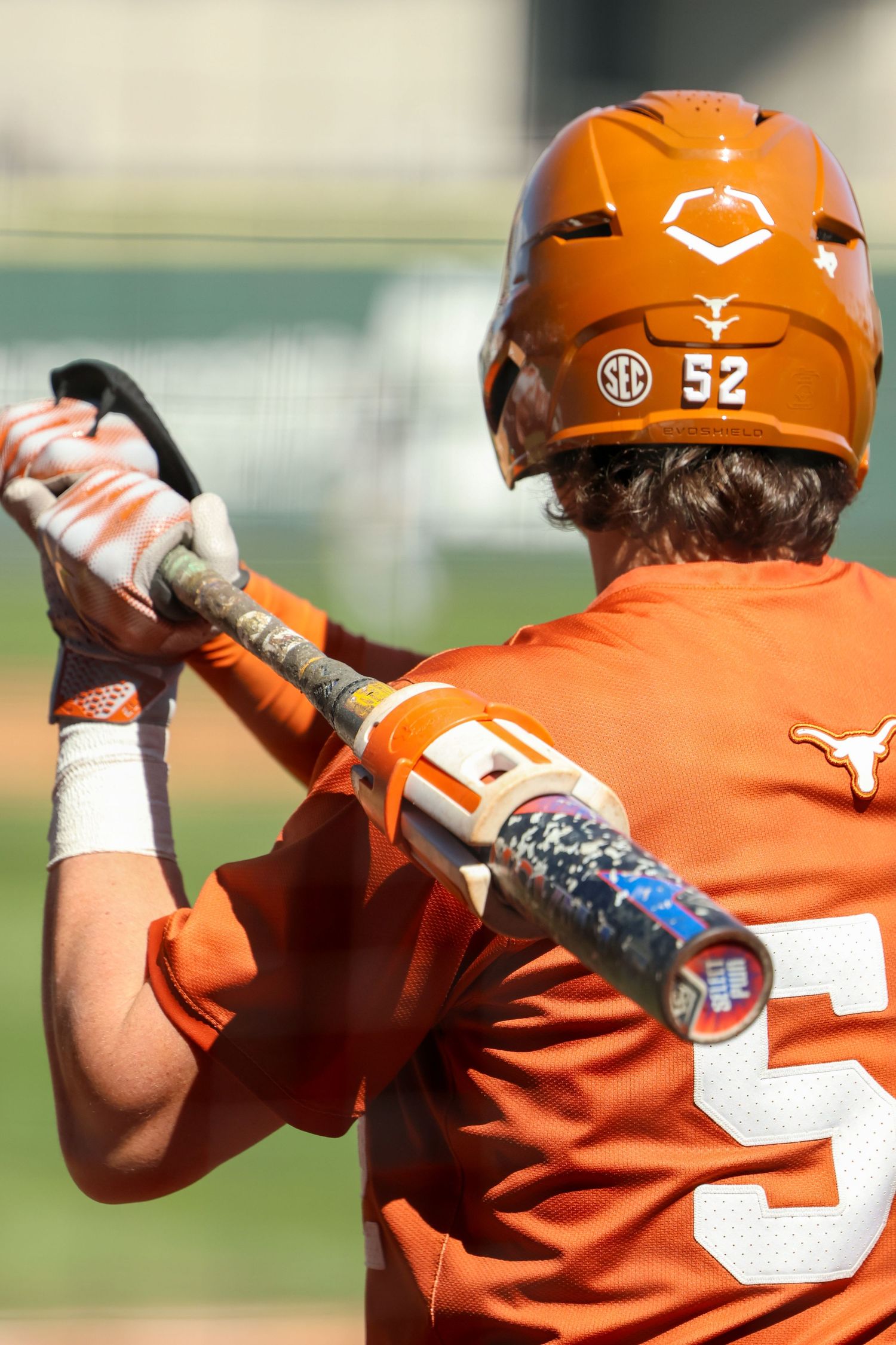 Baseball player in orange Texas Longhorns uniform with number 52 takes batting stance during game.