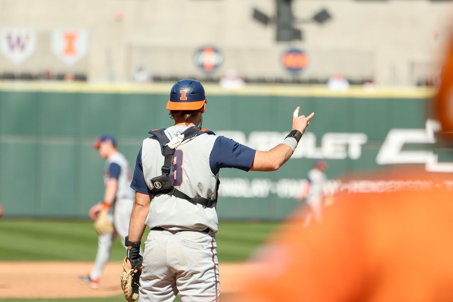 Baseball catcher signals to pitcher during game with stadium wall and Chevrolet advertisement in background.