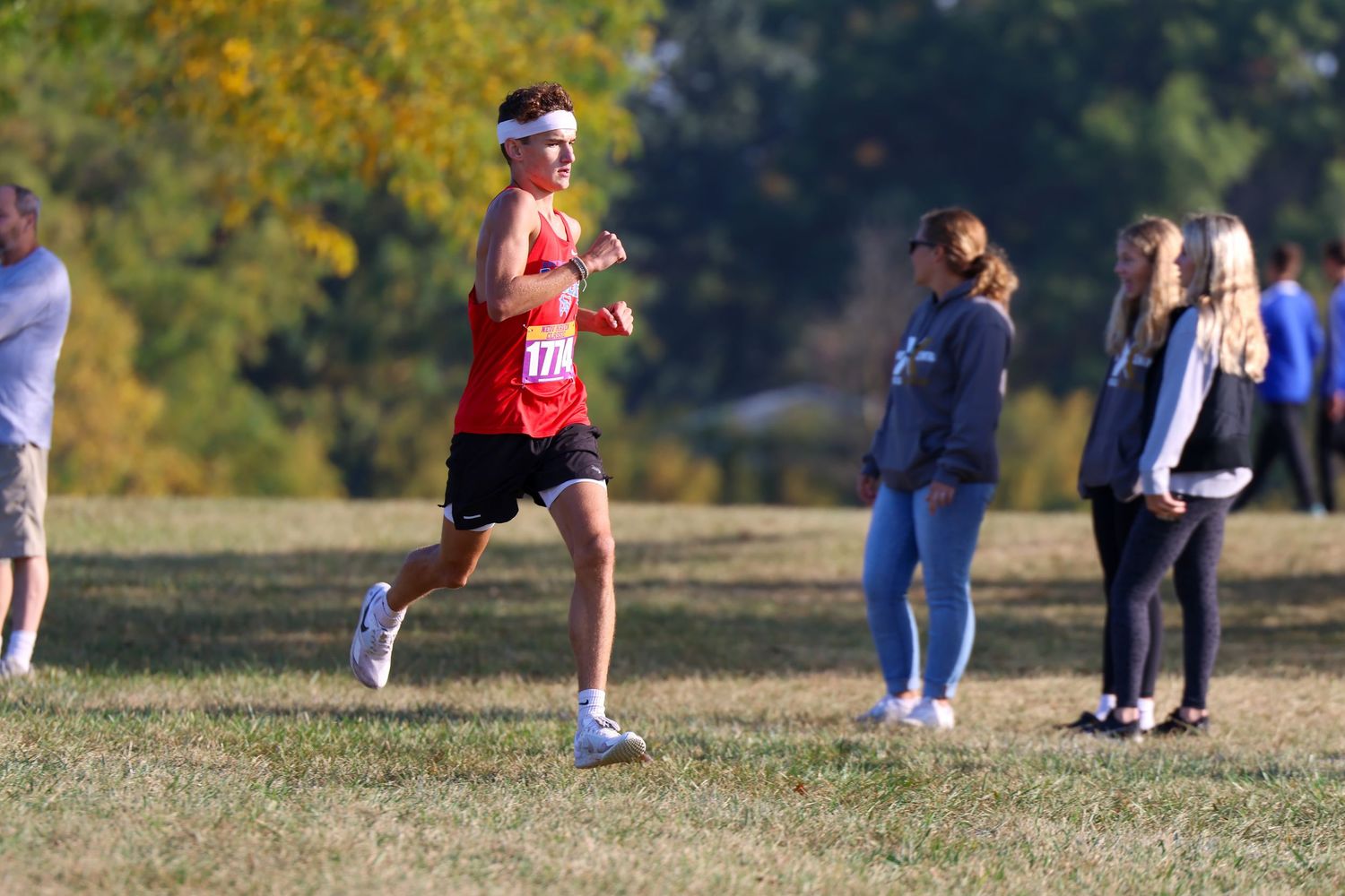 A runner in red athletic gear competes on a cross country course while spectators watch from the sidelines.