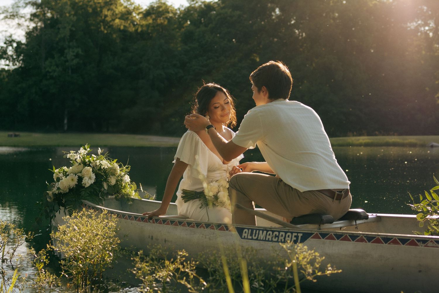 Couple sharing a romantic moment in a canoe decorated with white flowers on a serene lake at sunset.