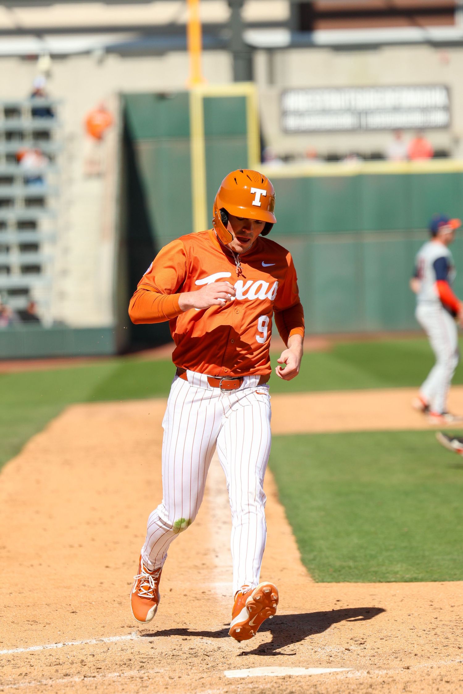 Baseball player in orange uniform and pinstripes runs down baseline during game at outdoor stadium.