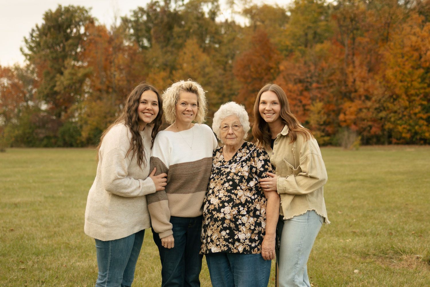 Four women multi-generational family portrait outdoors with vibrant autumn foliage background.