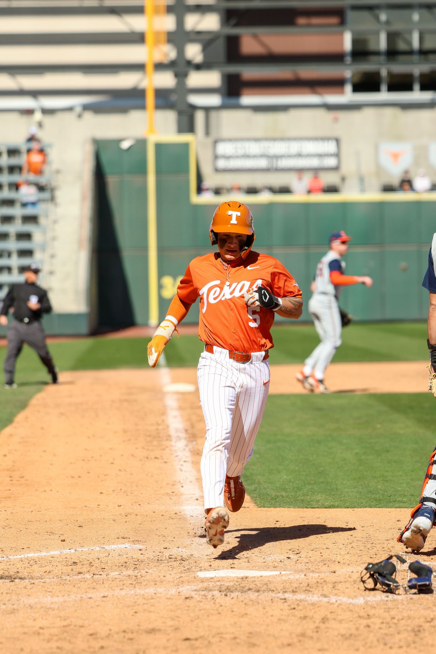 Baseball player in orange Texas Longhorns uniform runs toward home plate during college baseball game.