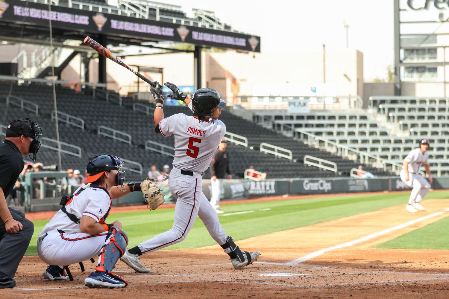 Baseball player swings bat at home plate during sunset game at empty stadium.