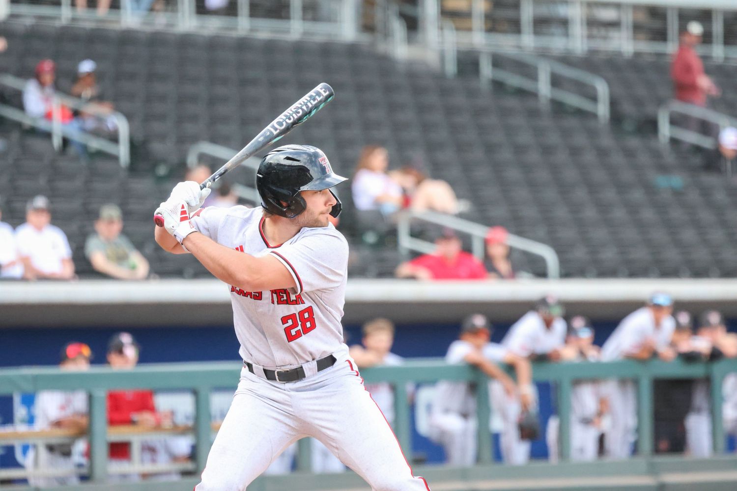 Baseball batter in white uniform stands at bat during professional game with empty stadium seats in background.