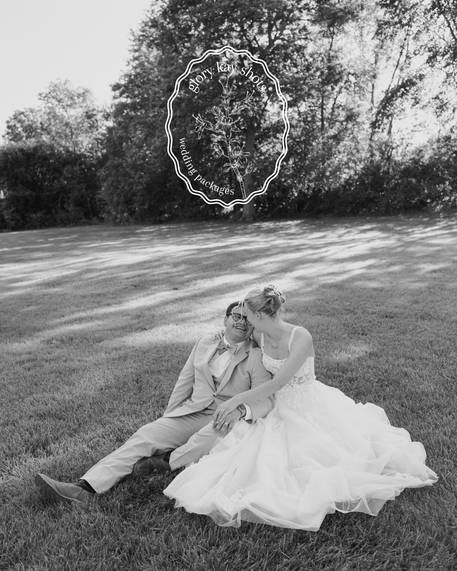 Black and white photo of a bride and groom sitting together on a grassy lawn in wedding attire.