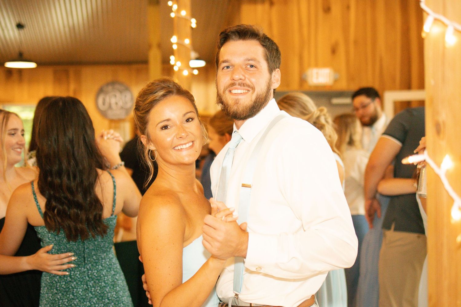 Smiling bride and groom share a dance at rustic barn wedding reception with string lights.