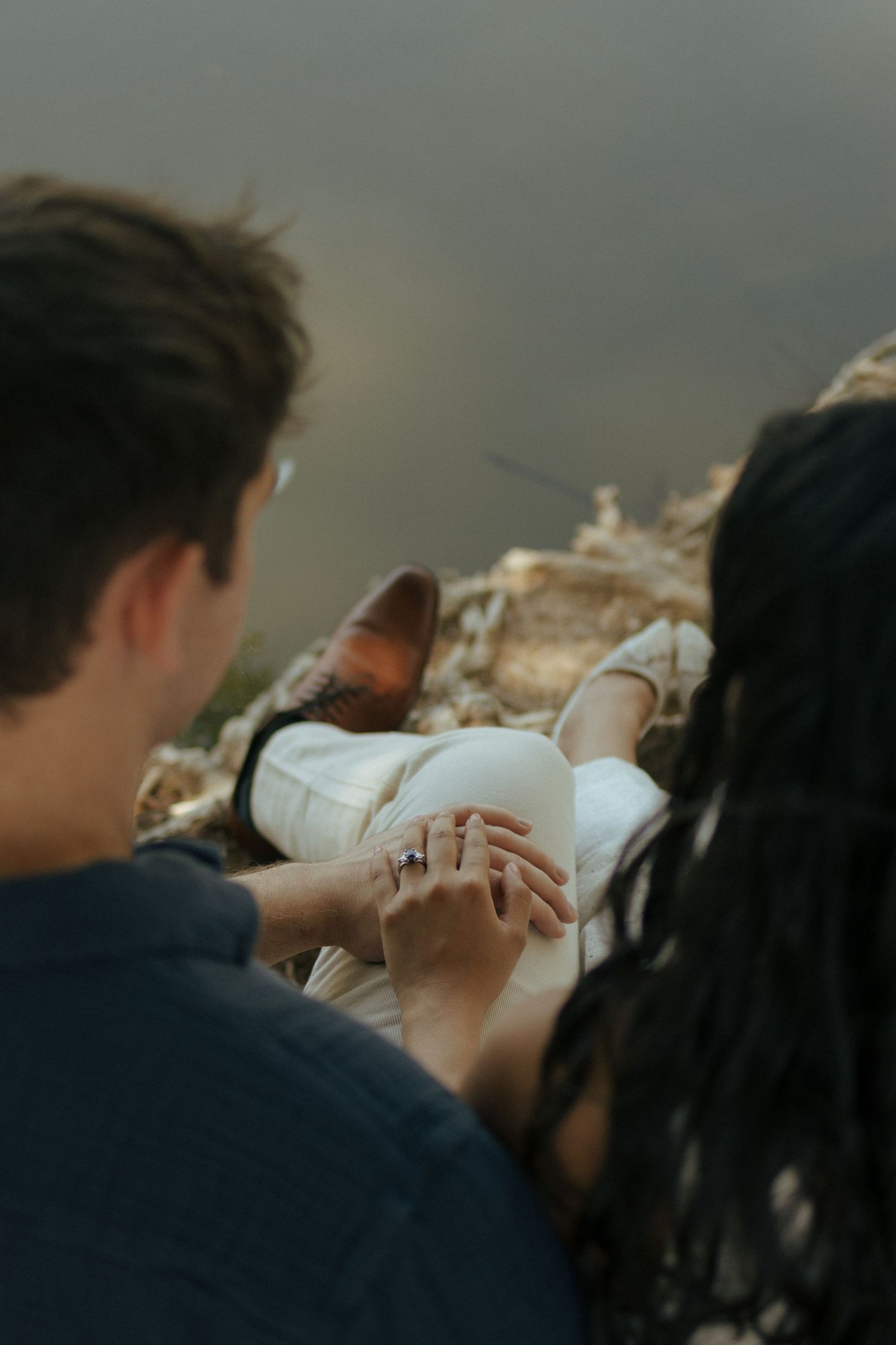 A couple holds hands while sitting together on rocks during sunset, creating an intimate moment in nature.