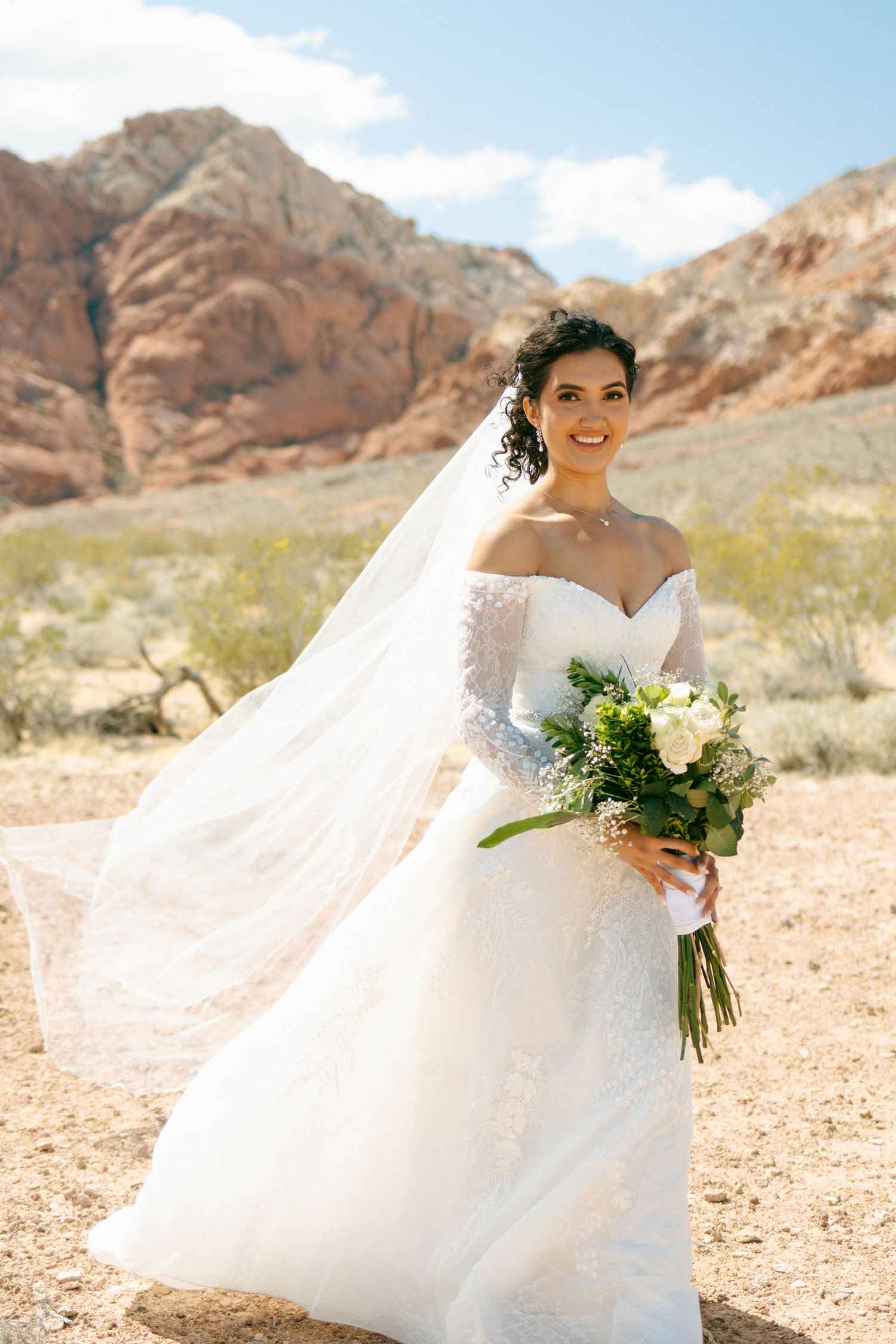 White wedding gown flowing gracefully in desert breeze at Red Rock Canyon with mountains in background.