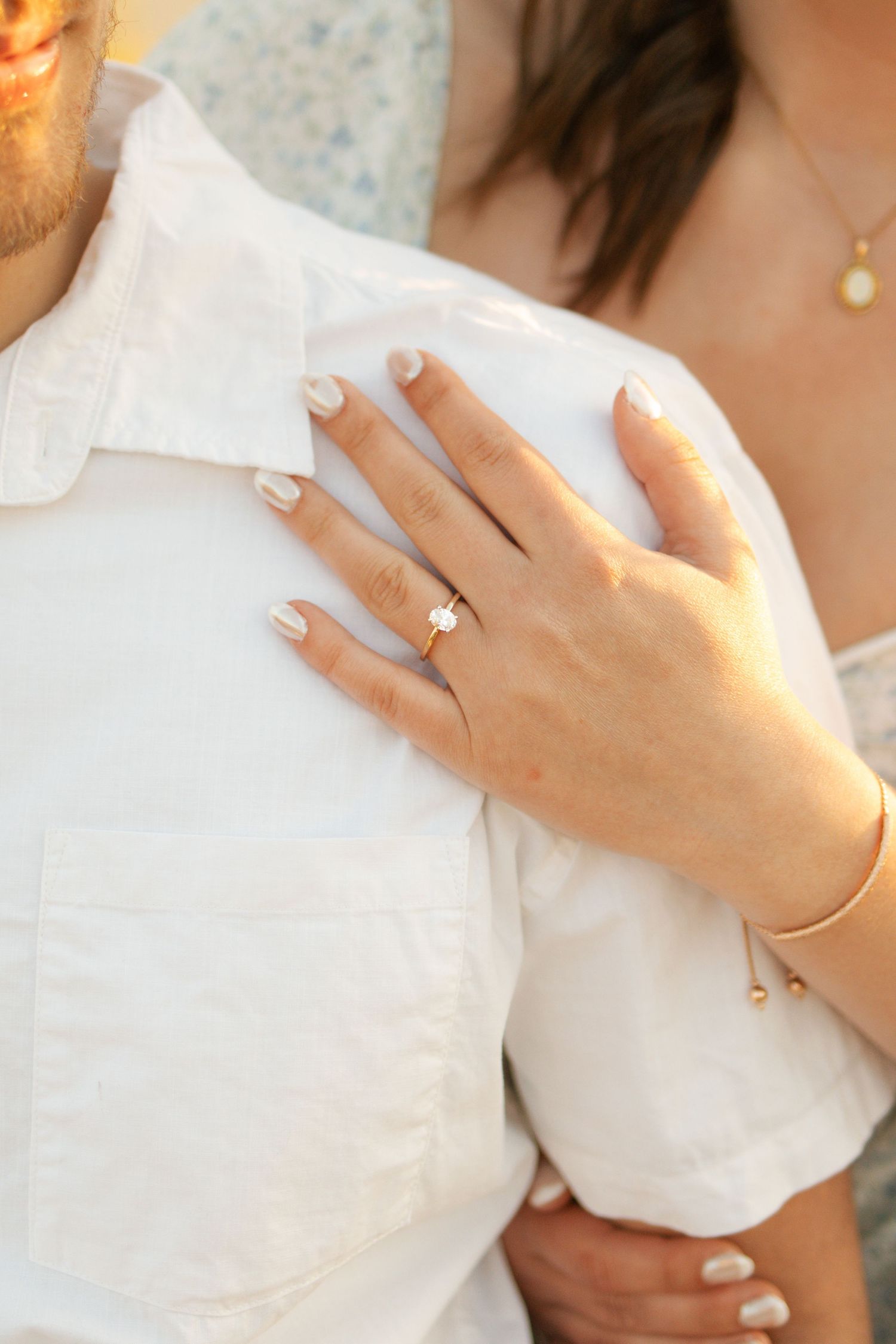Close-up of a woman's hand with a gold solitaire engagement ring resting on a man's white shirt.