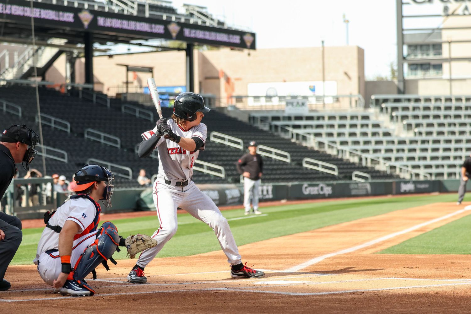 Baseball batter stands ready at home plate while catcher crouches behind during a sunny afternoon game.