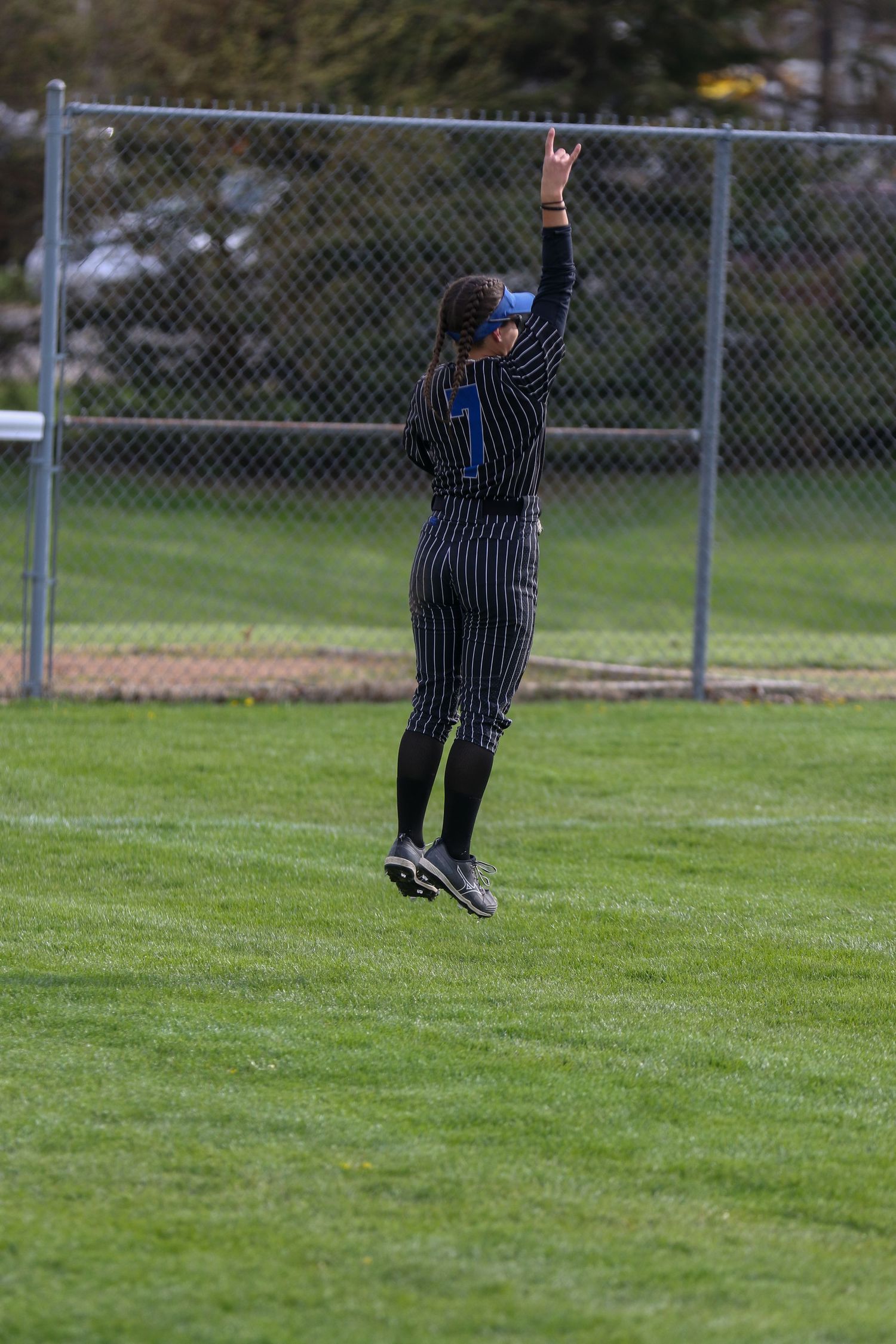 Baseball outfielder in striped uniform leaps high to catch a fly ball on a grassy field.