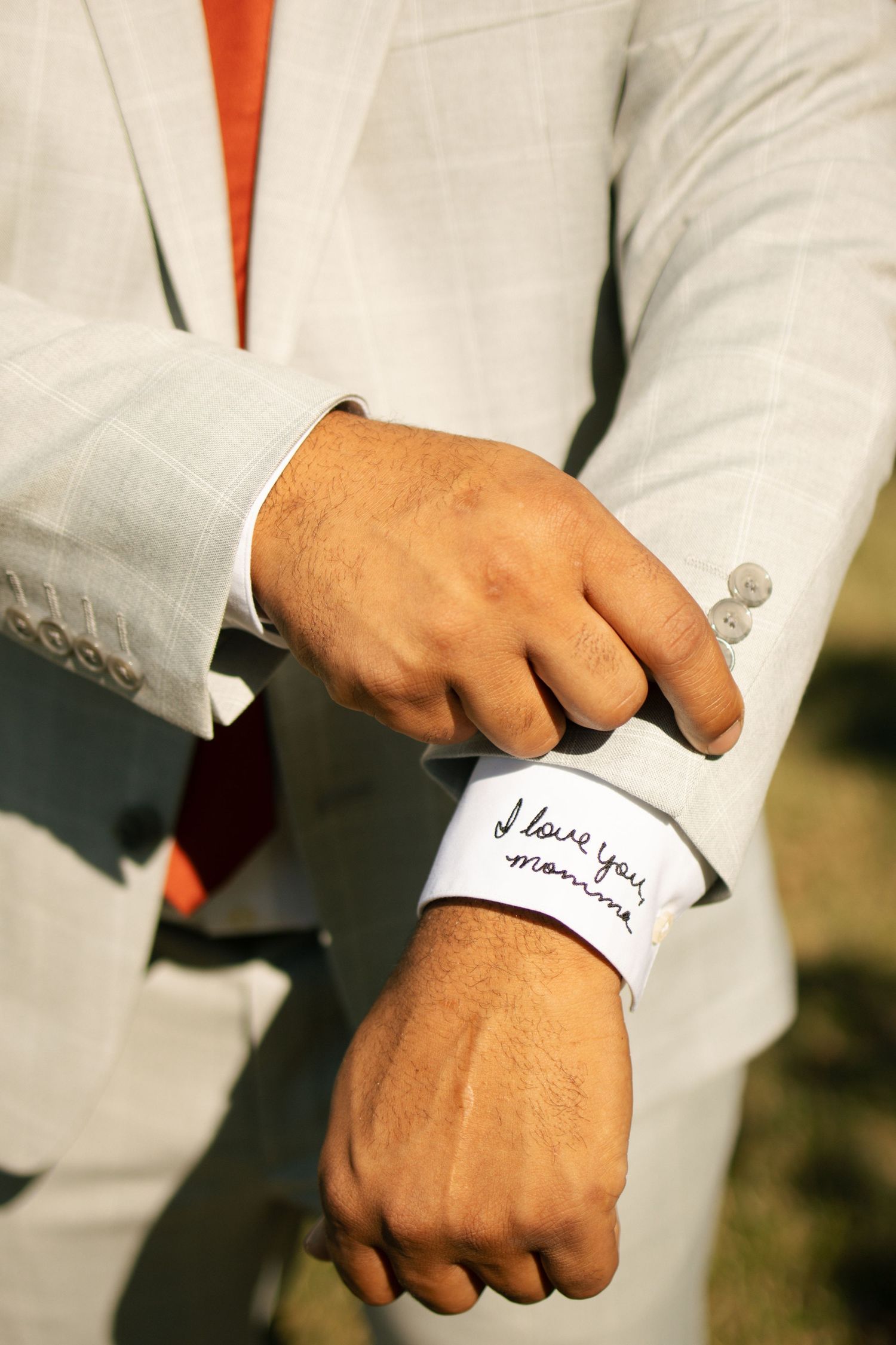 Groom in white linen suit adjusting cufflinks revealing I love you mama written on shirt cuff.
