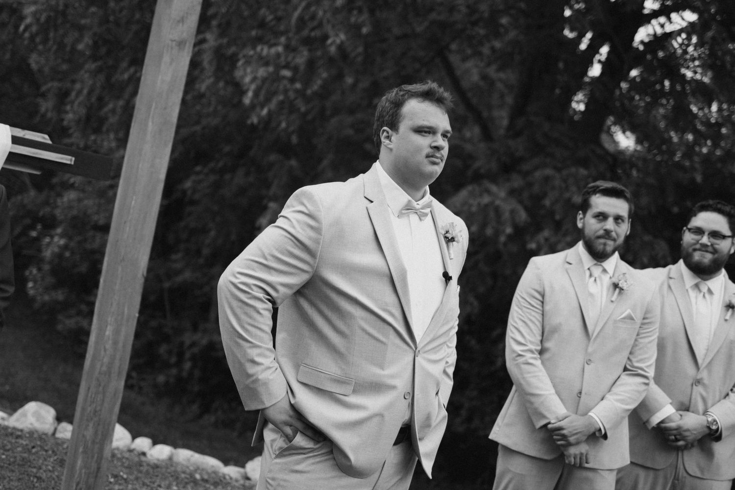Black and white photo of groomsmen in light suits at an outdoor wedding ceremony.