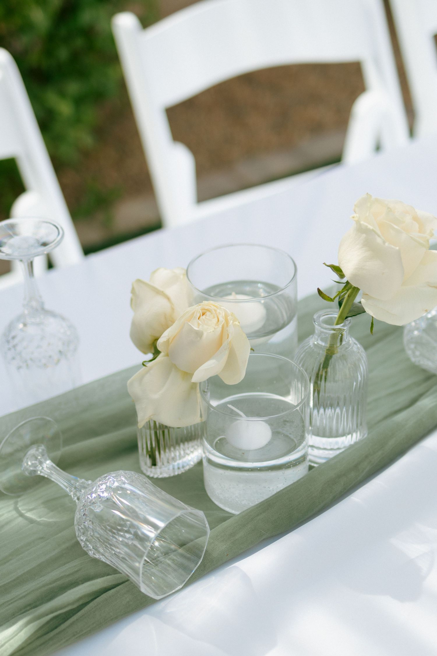 White roses and glass vases decorate an elegant table setting with sage green accents.