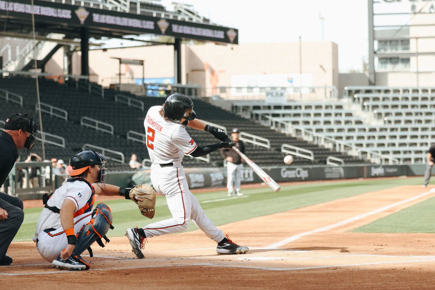 Baseball player swings the bat at home plate during a game while the catcher crouches behind home base at stadium.