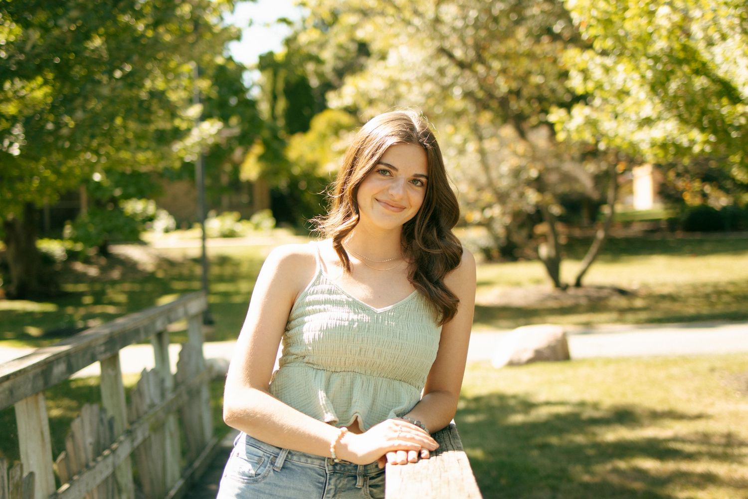 Young woman in white top leaning on wooden bridge railing in autumn park setting.
