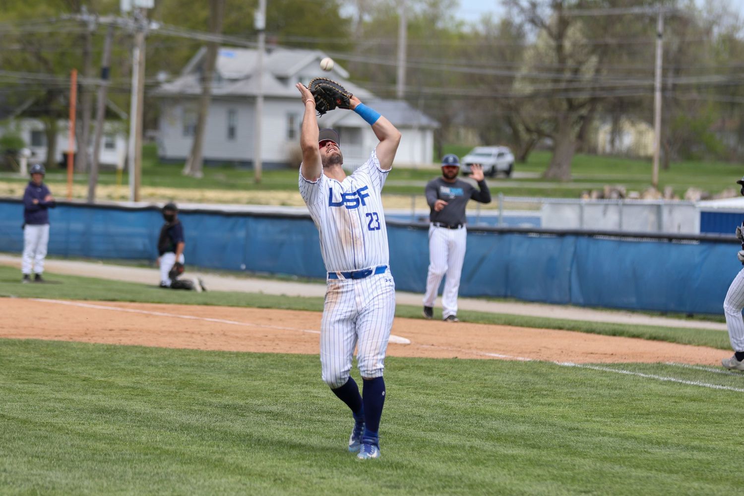 Baseball player in white uniform stands ready on the pitcher's mound during a game on a sunny spring day.