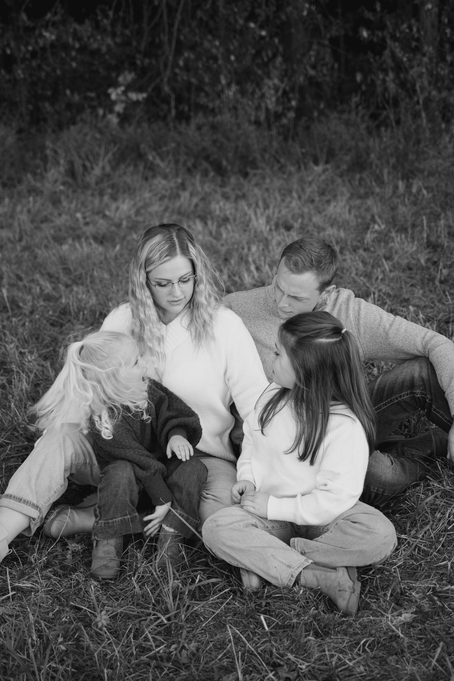 Black and white family photo of parents and two children sitting together on grass in a peaceful outdoor setting.