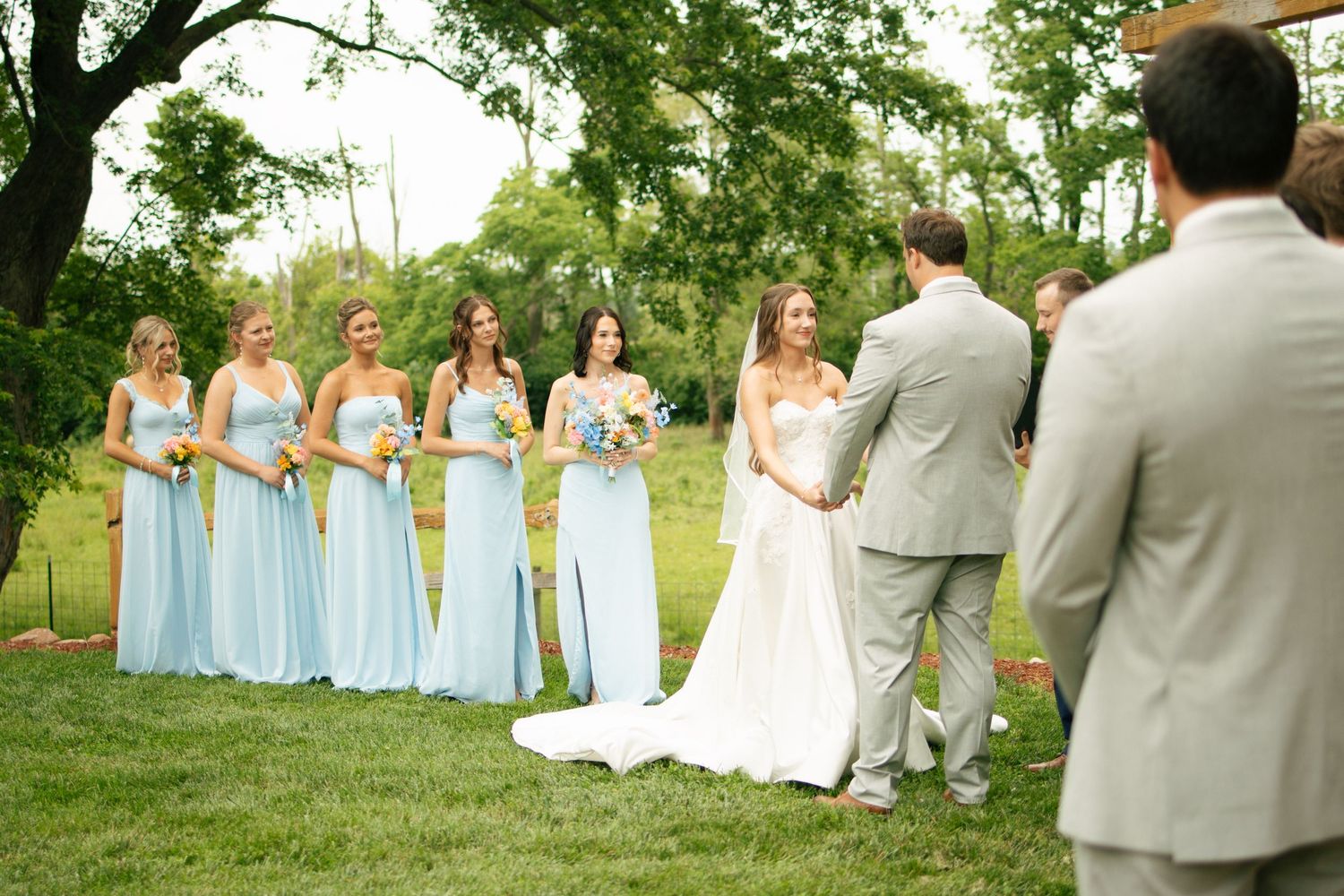 Bride and groom share first look outdoors with bridesmaids in light blue gowns at garden wedding.