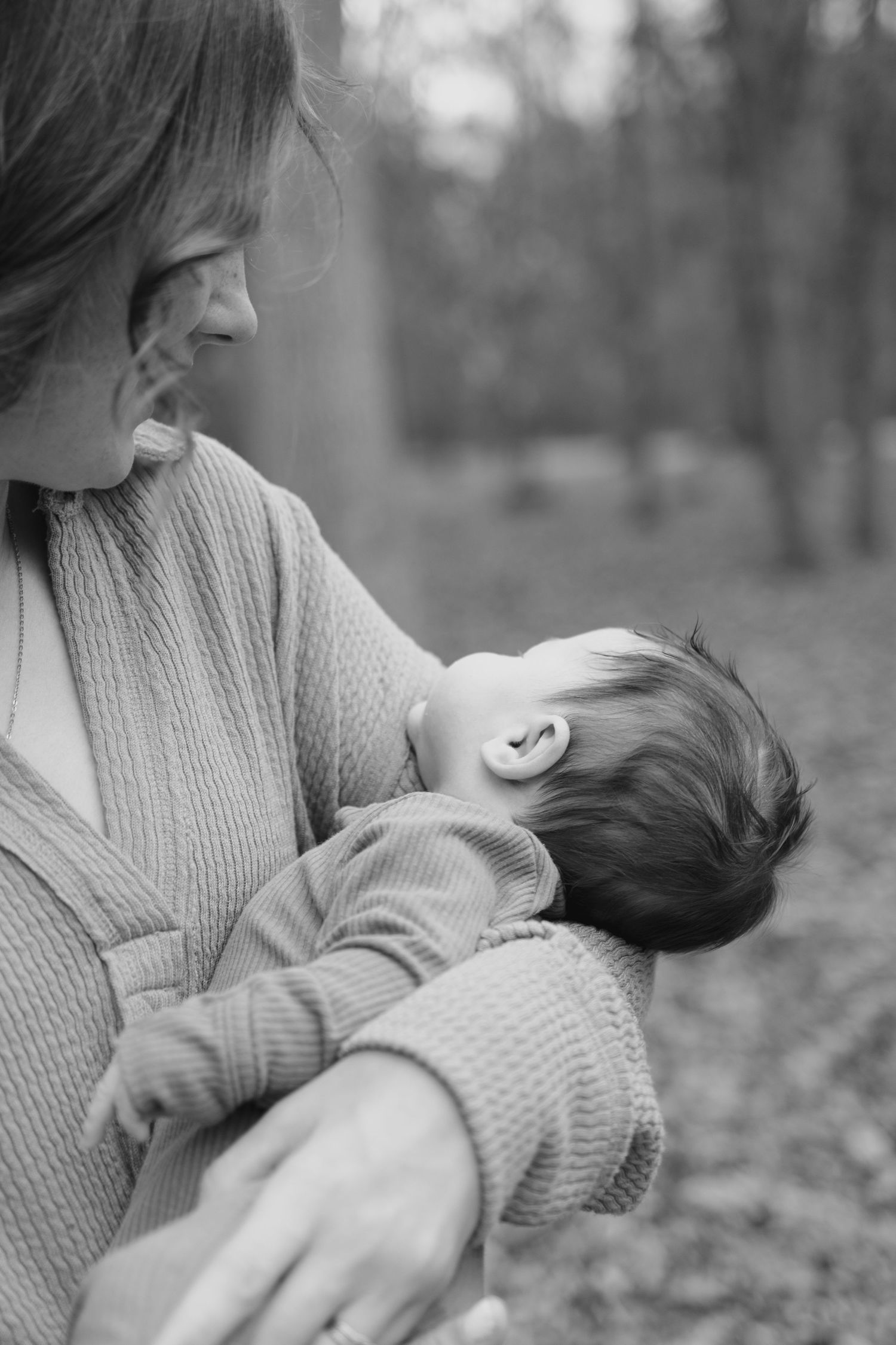 Black and white photo of a mother tenderly holding and breastfeeding her newborn baby outdoors in nature.