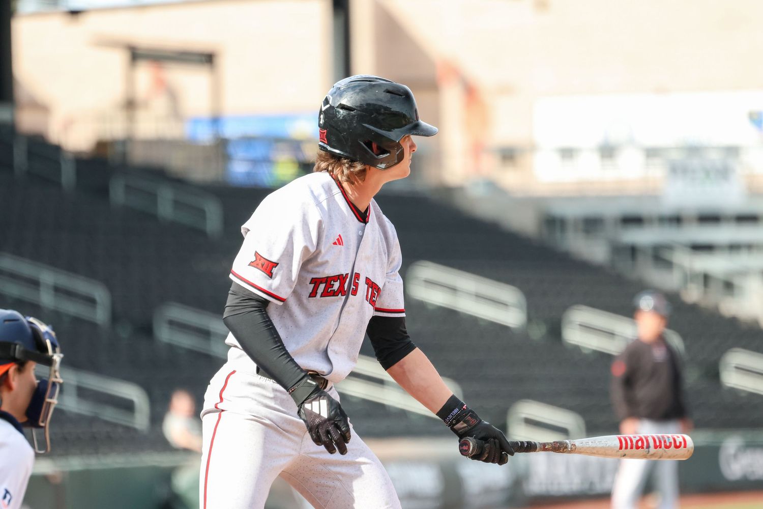 A baseball player in white uniform with red trim stands at bat holding a Wilson baseball bat during a game.